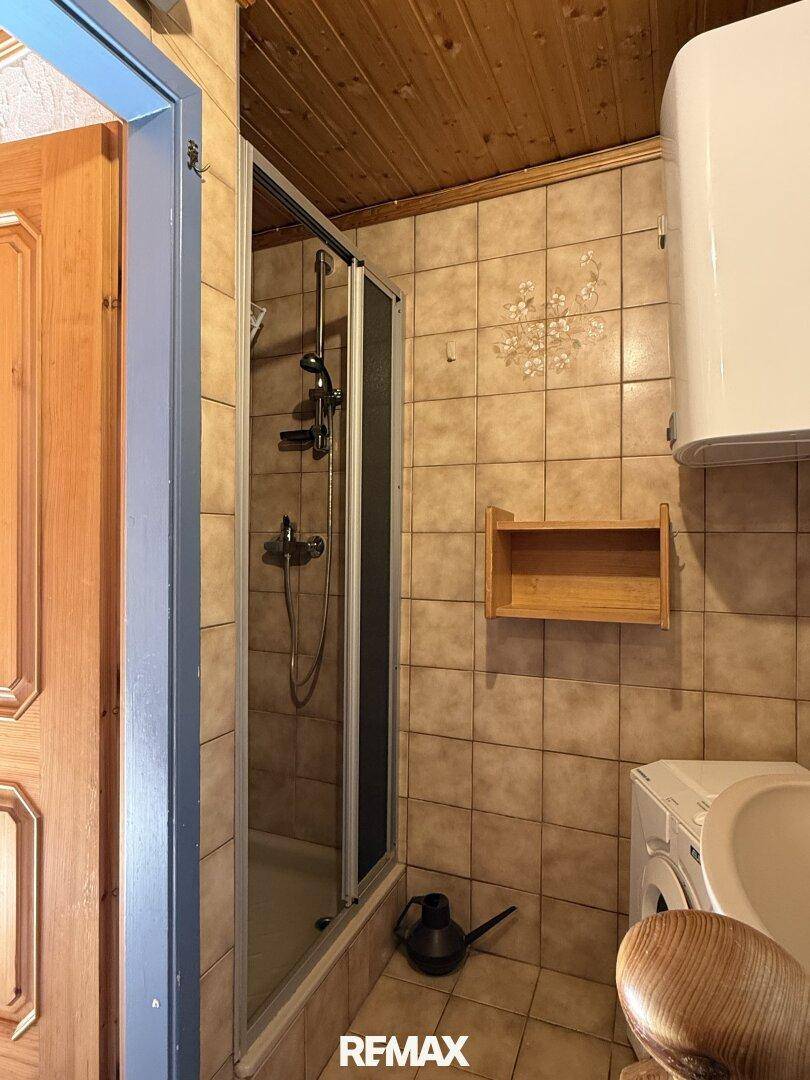 Kleines Badezimmer mit Duschkabine, Fliesenboden und Waschmaschinenanschluss.