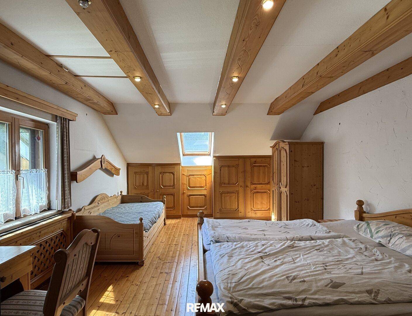 Geräumiges Schlafzimmer mit Holzbalken, mehreren Betten und Dachfenster für natürliches Licht.