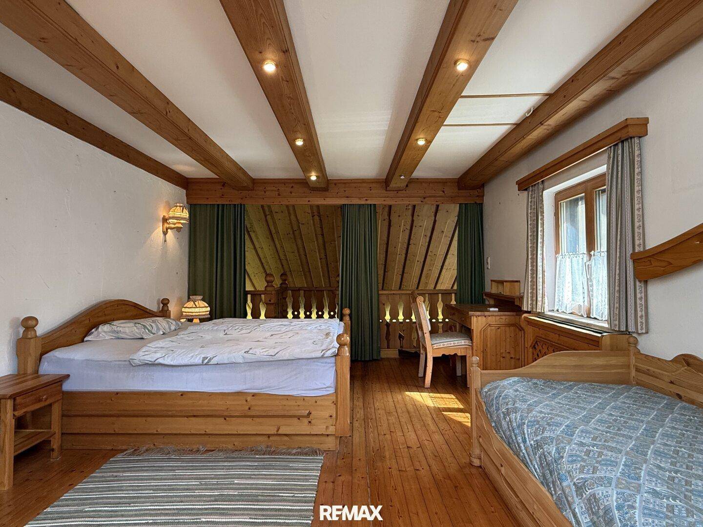 Helles Schlafzimmer mit Holzbalken, Doppelbett und Zugang zu einem Balkon.
