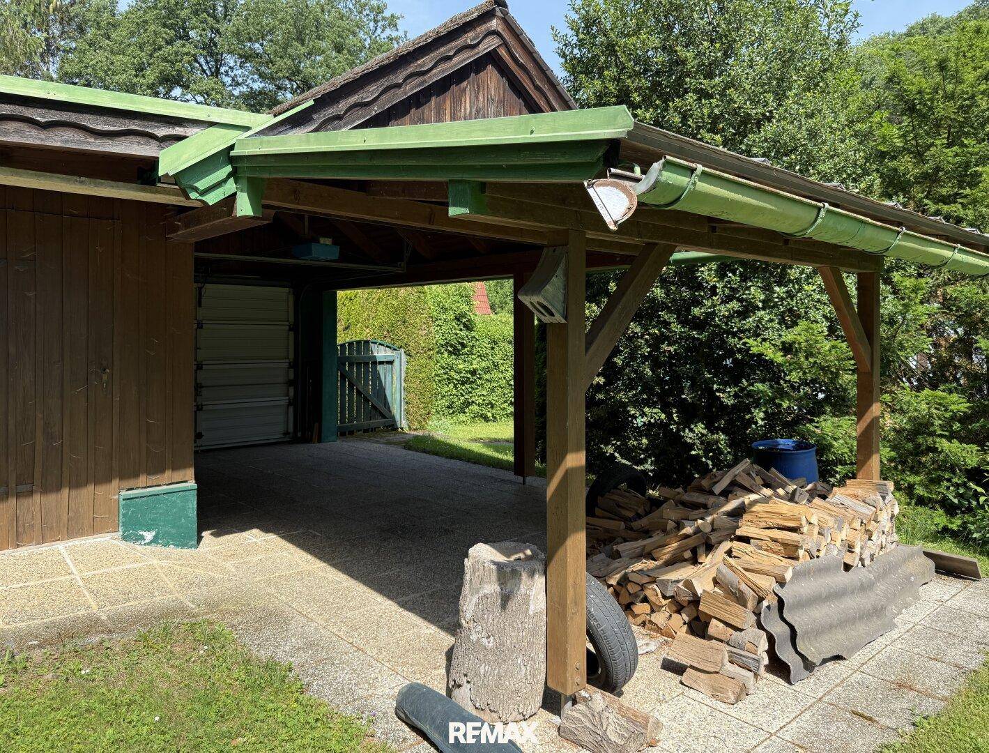 Überdachter Carport-Bereich mit Holzstapel und Zugang zur Garage oder Abstellraum.