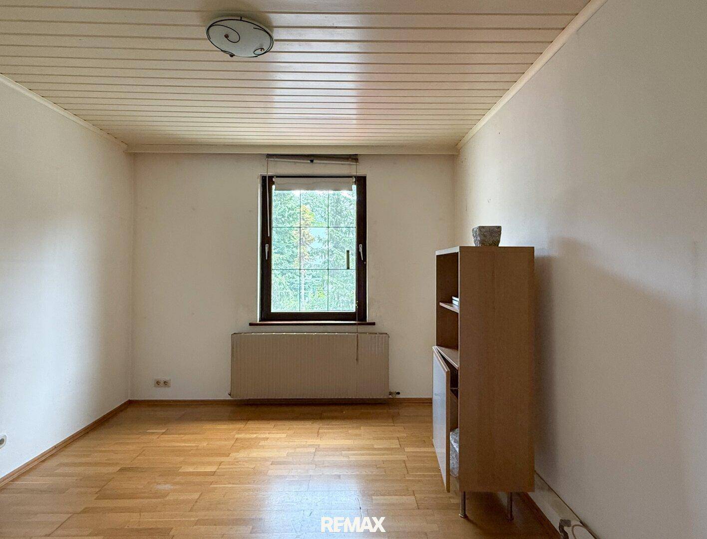 Helles Zimmer mit Parkettboden, weiß gestrichenen Wänden und Fenster mit Blick ins Grüne.