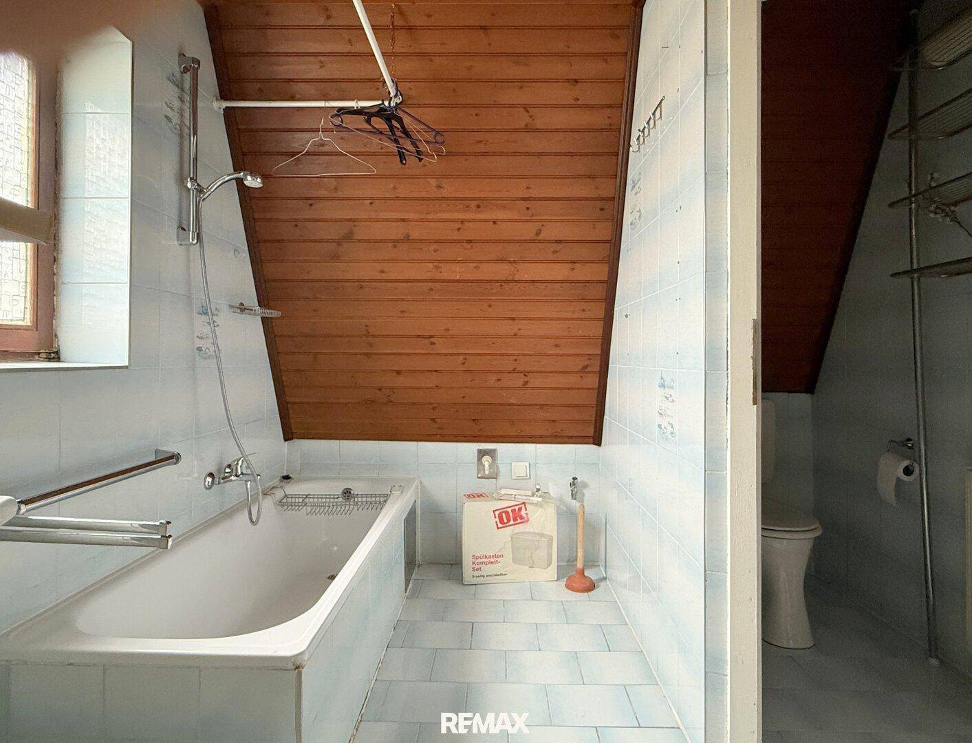 Badezimmer im Dachgeschoss mit Badewanne, Fliesen und schräger Holzdecke.