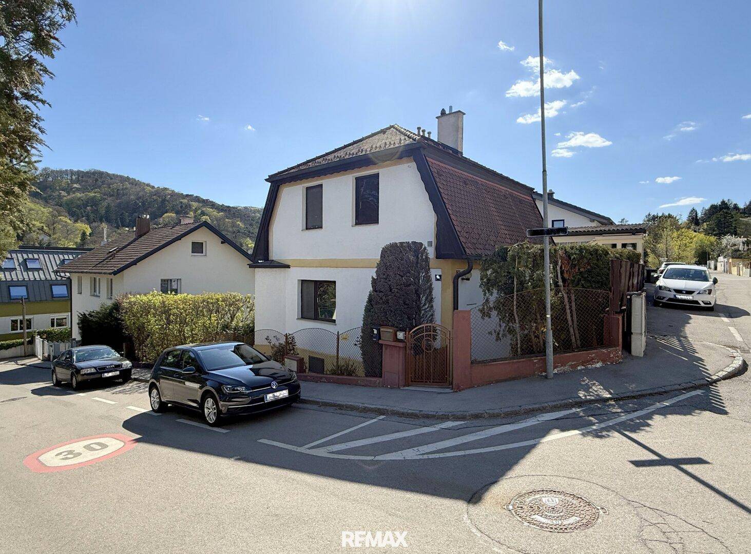 Ansicht des Hauses von der Straße mit Mansarddach und gepflegtem Vorgarten an einem sonnigen Tag.