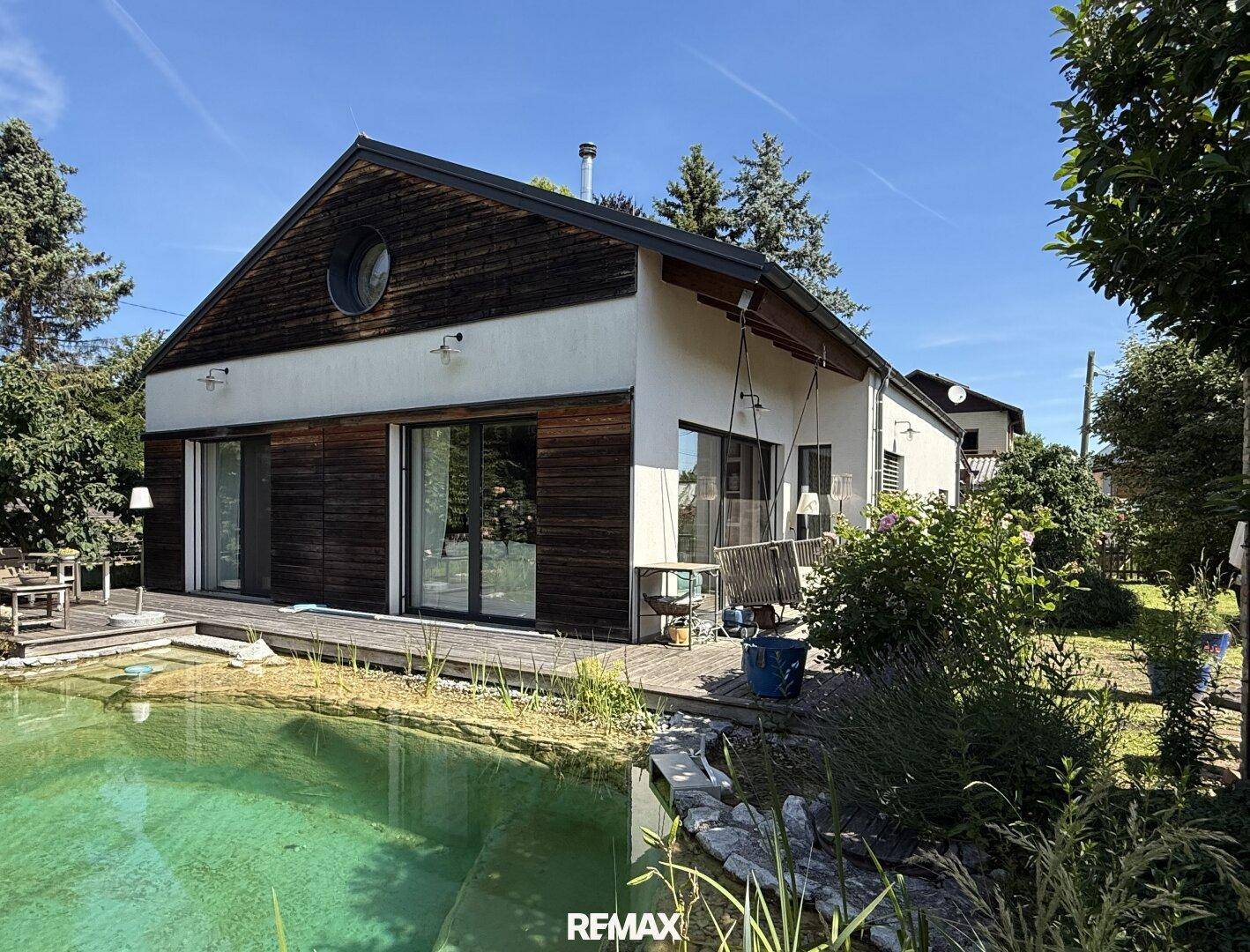 Modernes Haus mit Holzfassade und großem Naturpool im gepflegten Gartenbereich.