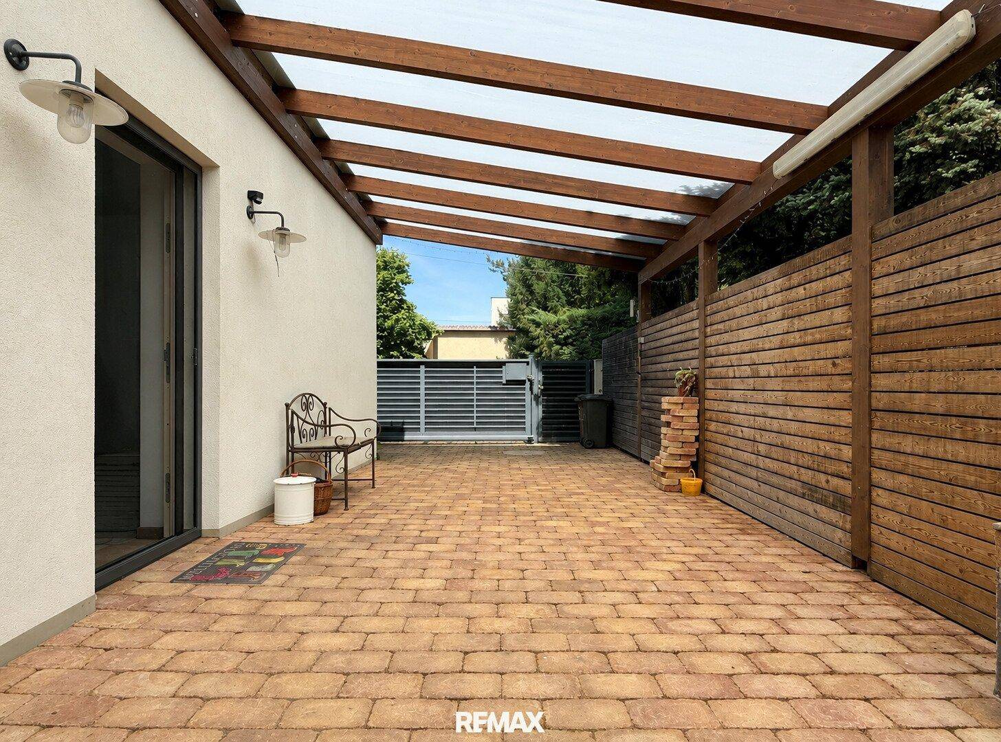 Überdachte Terrasse mit Ziegelpflaster und Holzzaun, ideal für entspannte Stunden im Freien.