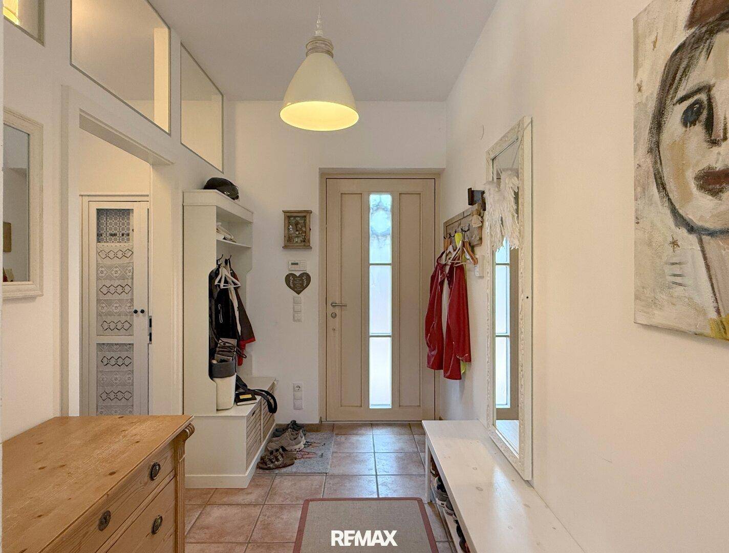 Heller Eingangsbereich mit Garderobe, Spiegel und Terrakottafliesen am Boden.