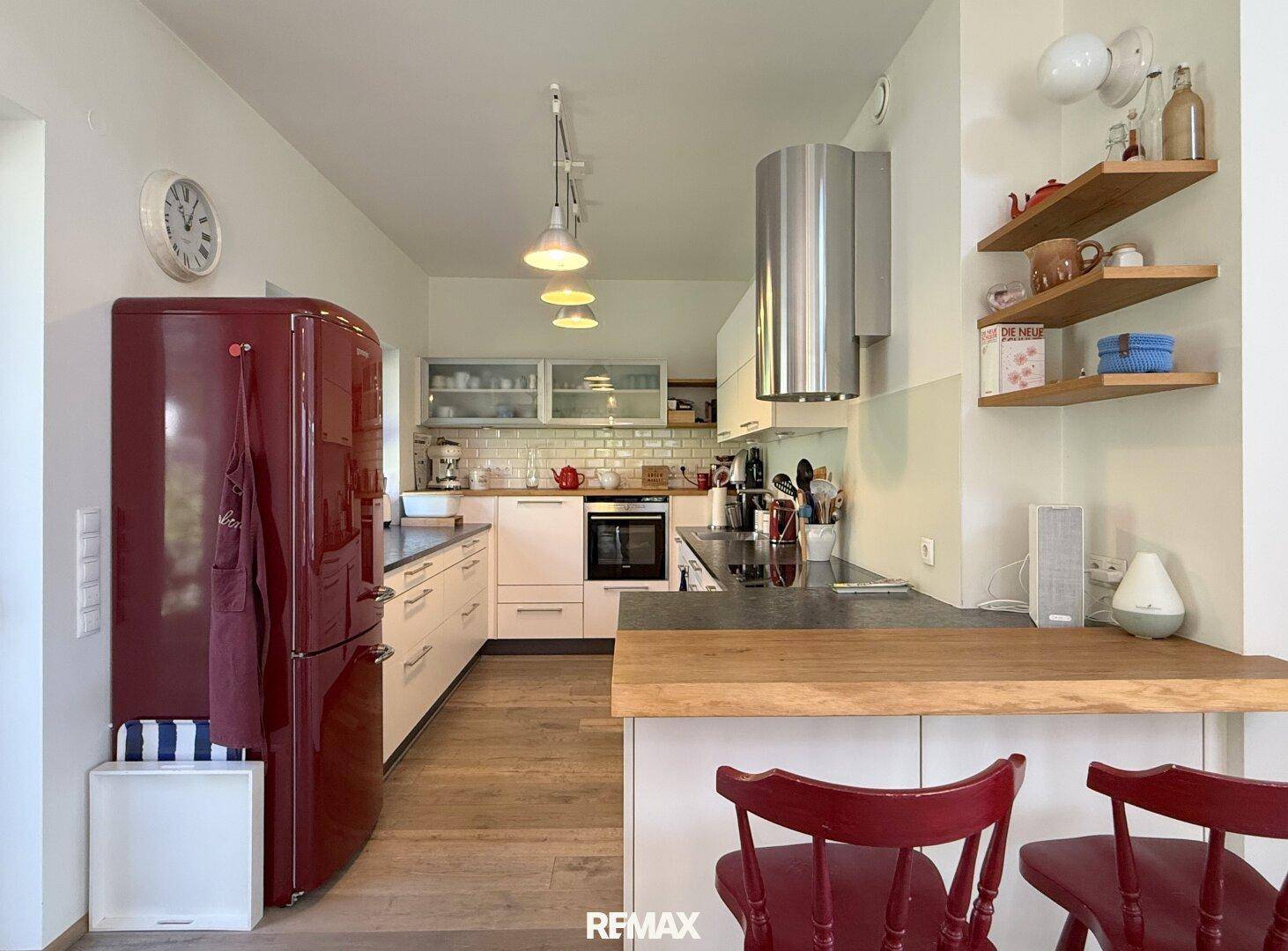 Moderne Küche mit rotem Retro-Kühlschrank, Holztheke und weißen Schränken.