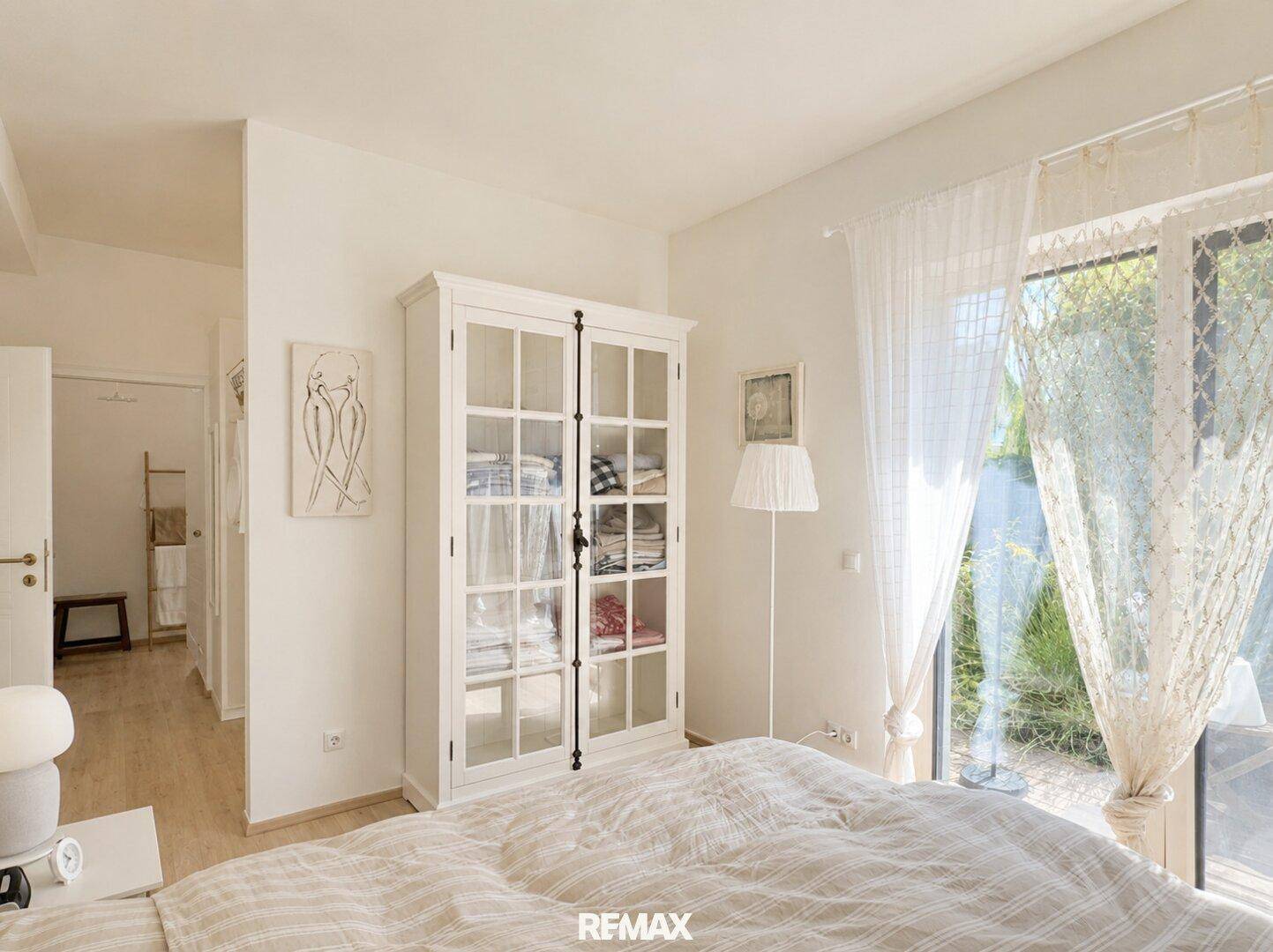 Helles Schlafzimmer mit Doppelbett, weißem Schrank und Zugang zum Garten.