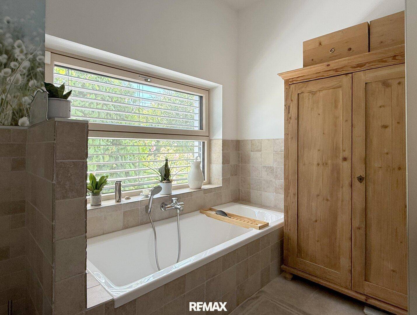 Badezimmer mit Badewanne, Fenster und rustikalem Holzschrank, in hellen Erdtönen.