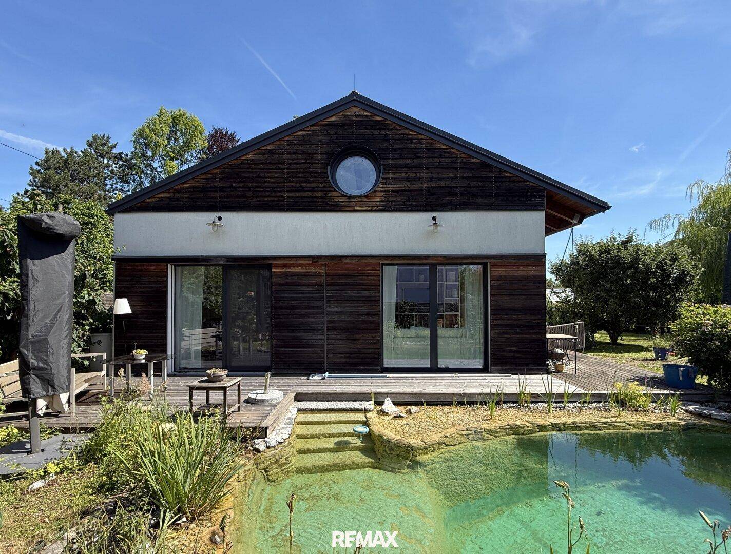 Modernes Haus mit Holzfassade, großzügiger Holzterrasse und einem natürlichen Schwimmteich.