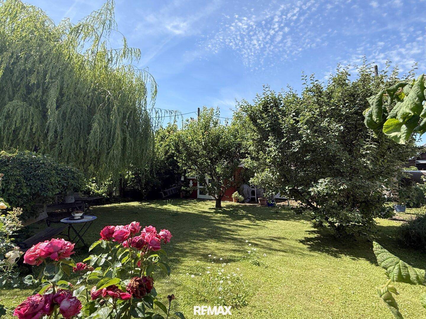 Großer, gepflegter Garten mit Rasenfläche, blühenden Rosen und altem Baumbestand.