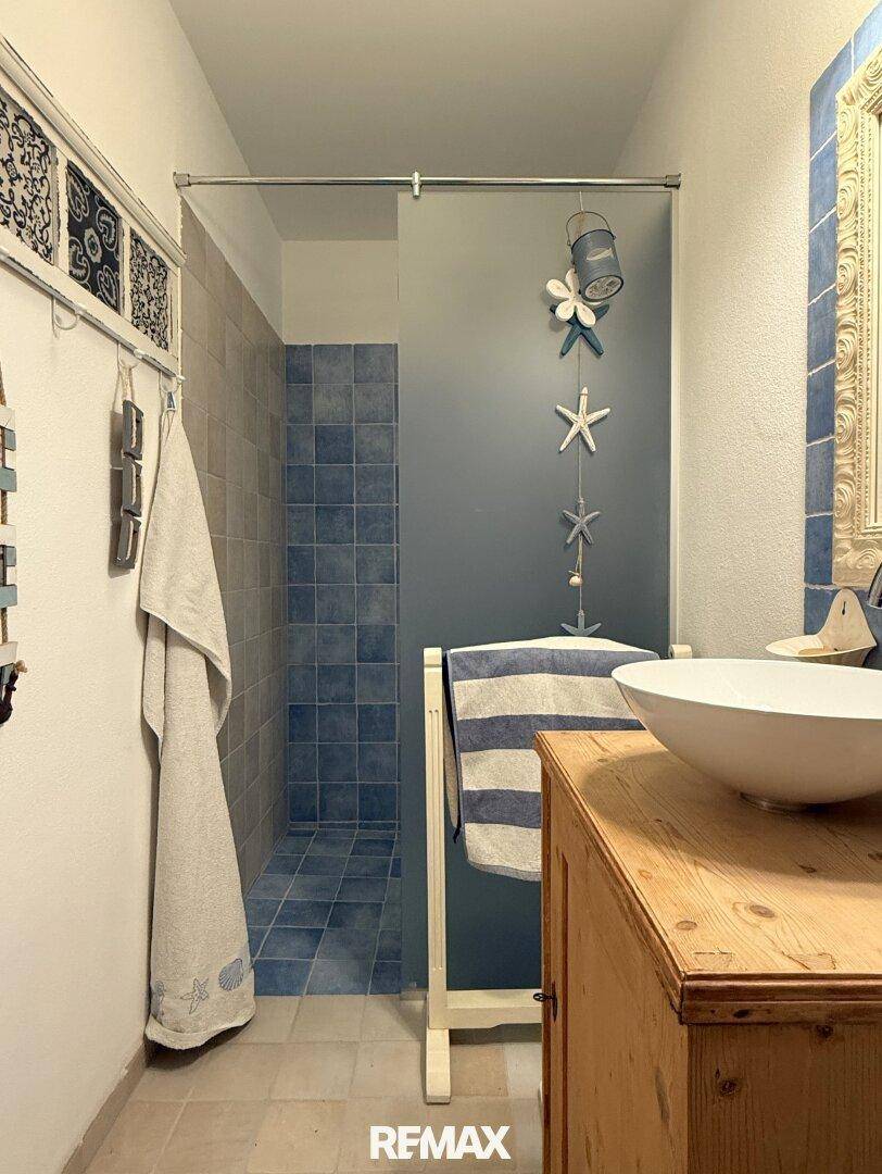 Badezimmer mit begehbarer Dusche, Waschbecken und maritimer Dekoration.