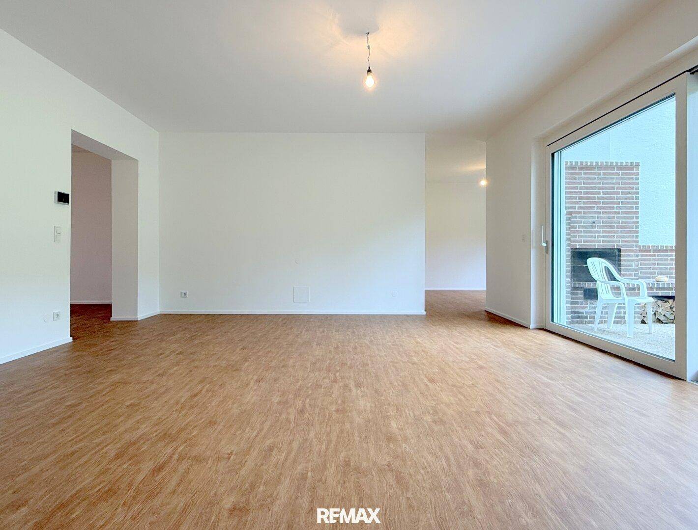Geräumiges, leeres Wohnzimmer mit Laminatboden und Zugang zur Terrasse.