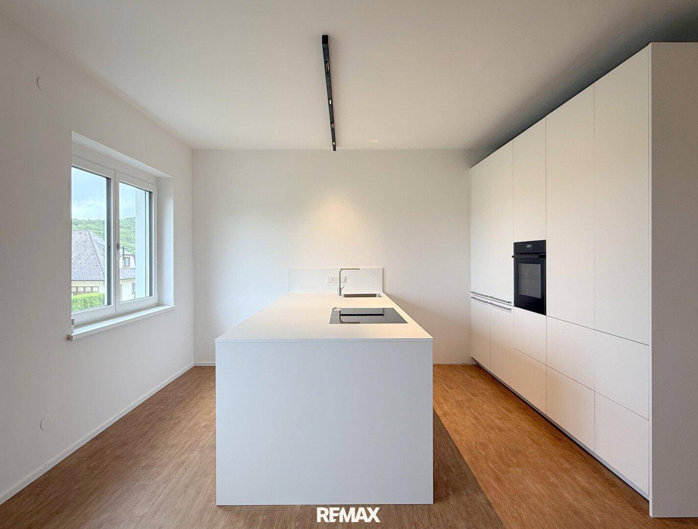 Moderne, minimalistische Küche mit weißen Schränken, integriertem Backofen und Kochinsel.