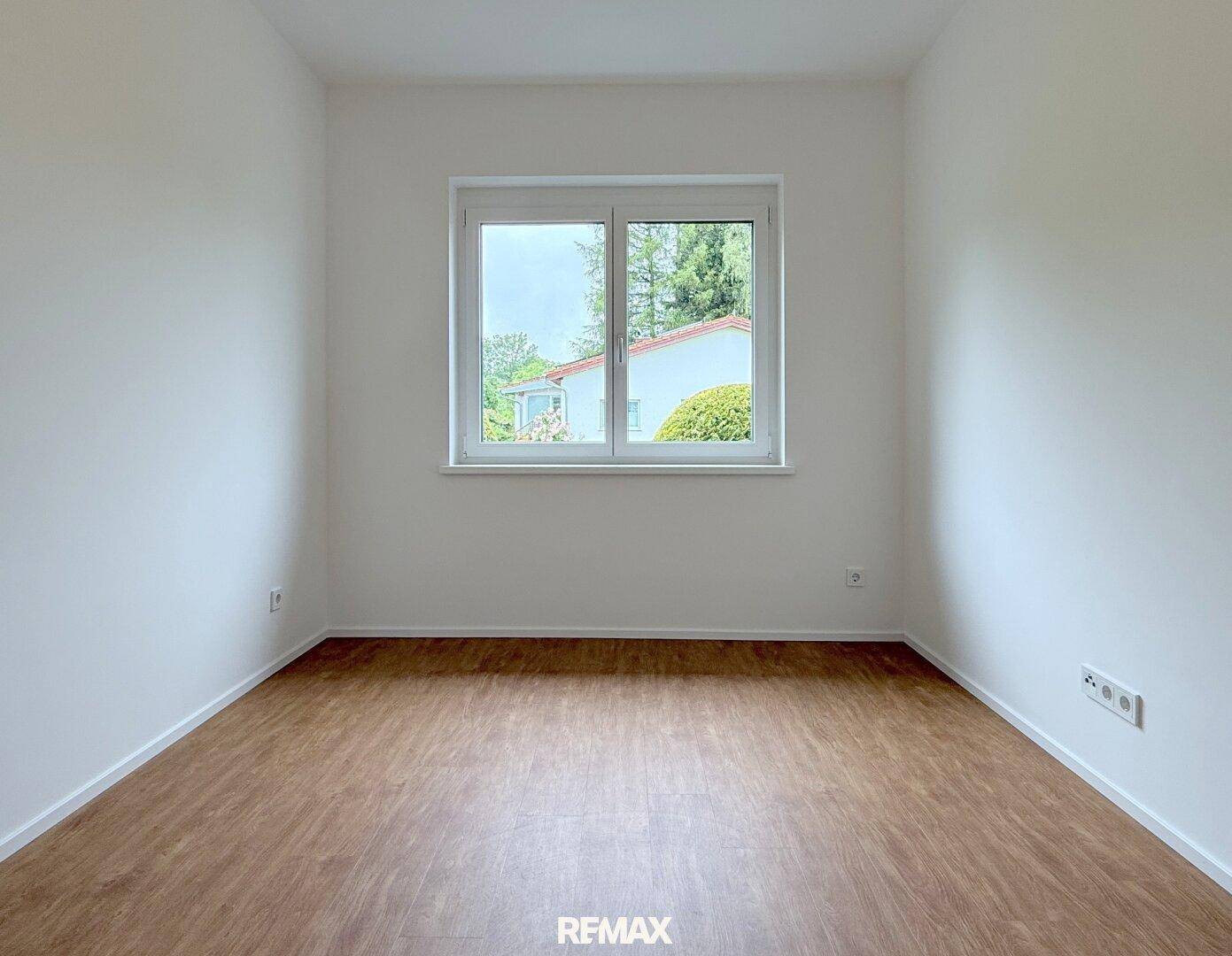 Ruhiges Schlafzimmer mit Laminatboden und einem großen Fenster mit Blick nach draußen.