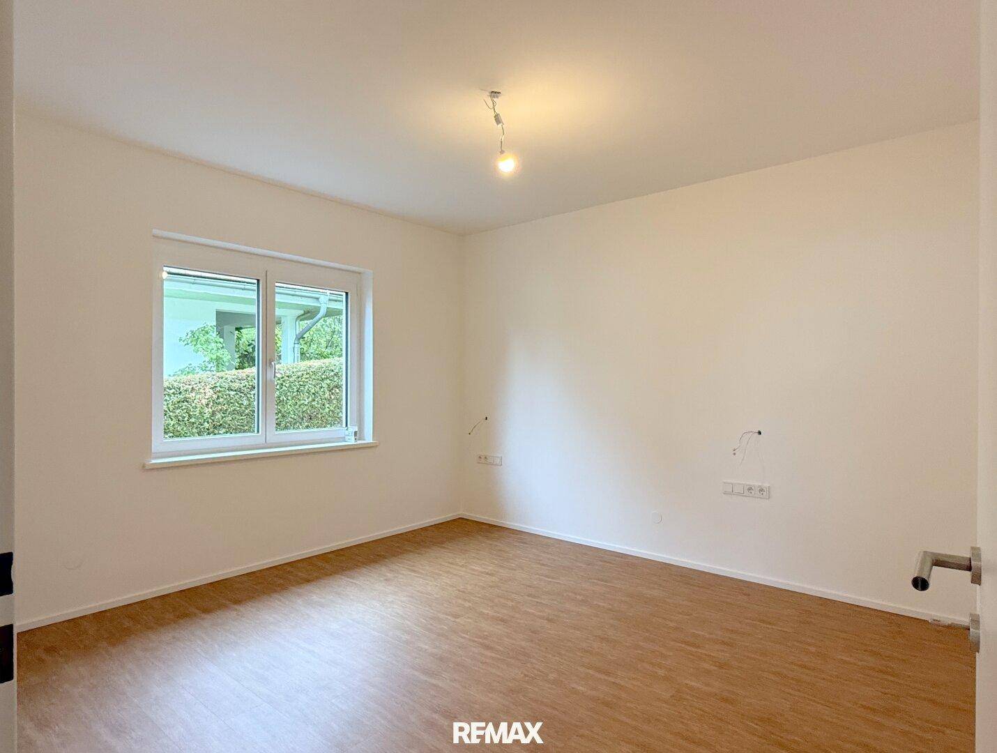 Helles Schlafzimmer mit Laminatboden und Fenster, das viel Tageslicht hereinlässt.