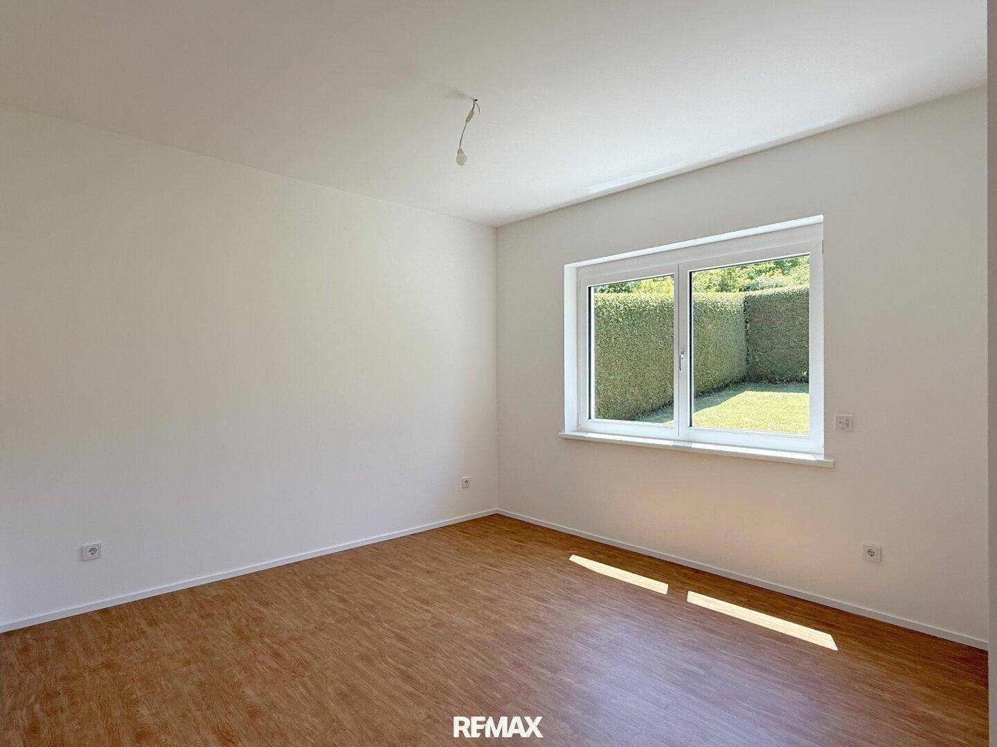 Helles Schlafzimmer mit Laminatboden und Fenster, das einen Blick auf die Hecke bietet.