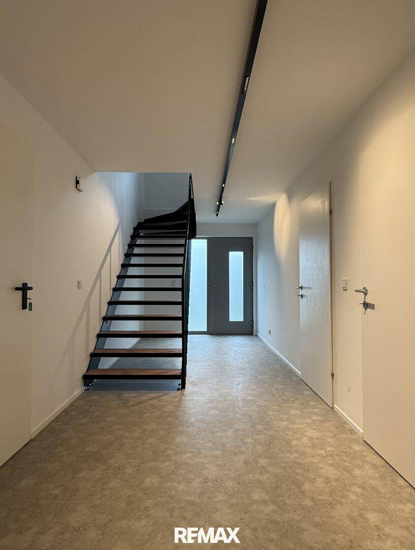 Heller Eingangsbereich mit moderner Treppe und Zugang zu verschiedenen Räumen.