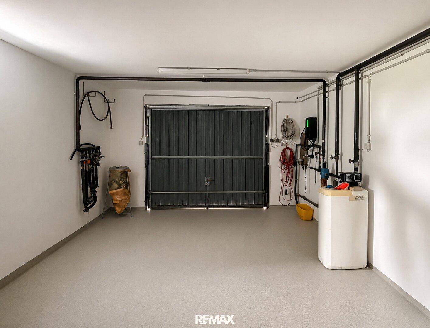 Geräumige Garage mit Rolltor und technischen Installationen, ideal für Fahrzeuge und Lagerung.