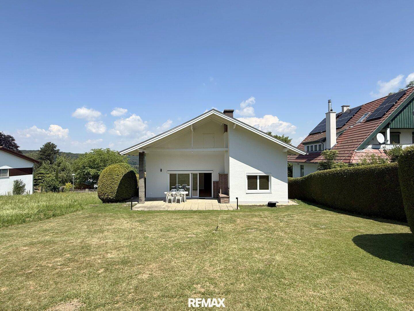 Rückansicht des Hauses mit weitläufigem Garten und Terrasse unter blauem Himmel.