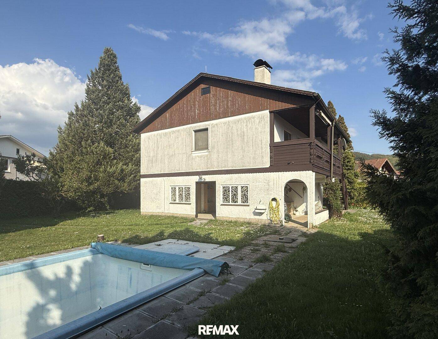 Gepflegter Garten mit Rasenfläche, Bäumen und einem leeren Swimmingpool neben dem Haus.