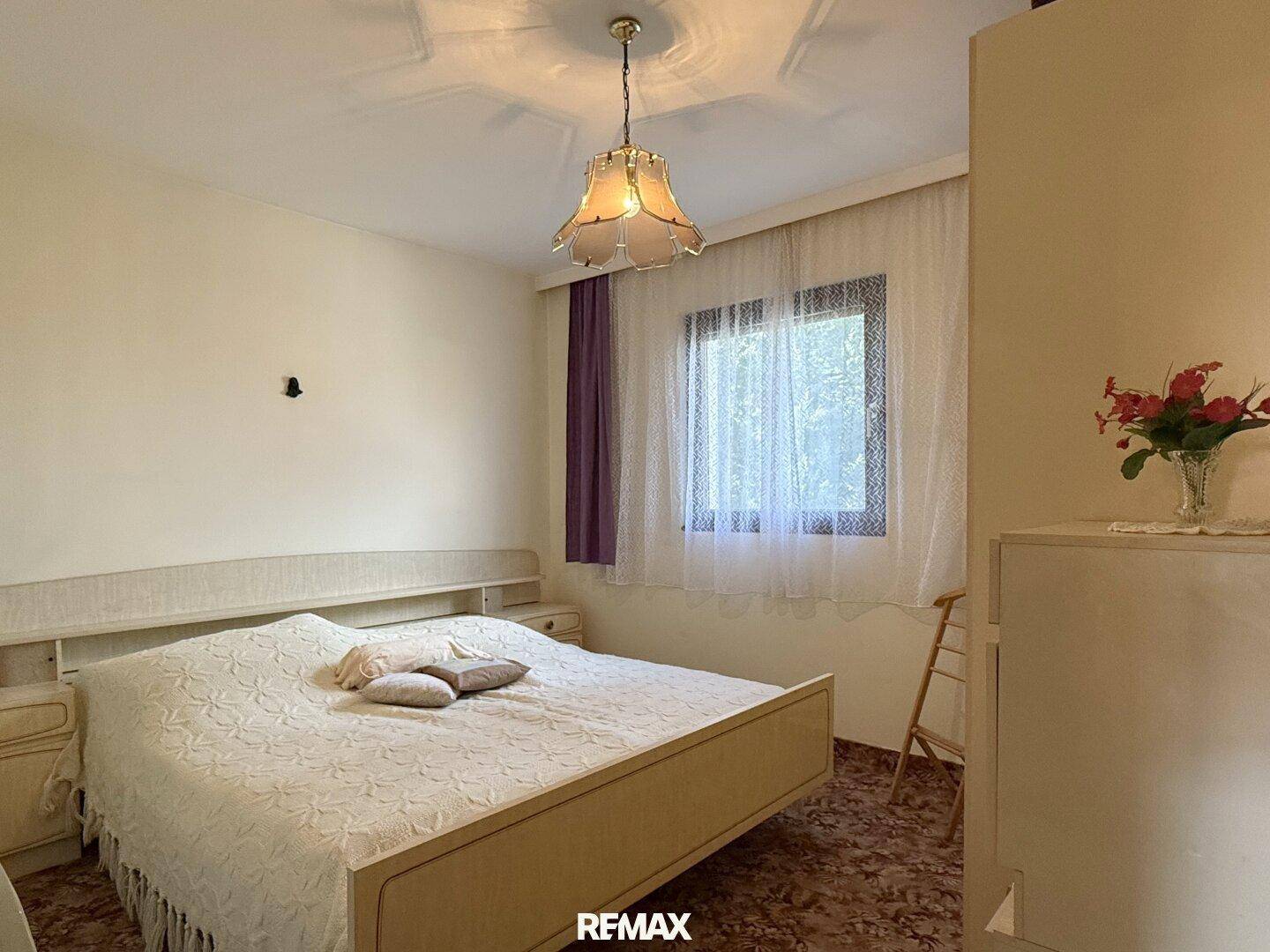 Schlafzimmer mit Doppelbett, Nachttischen und einem Fenster, das viel Tageslicht hereinlässt.