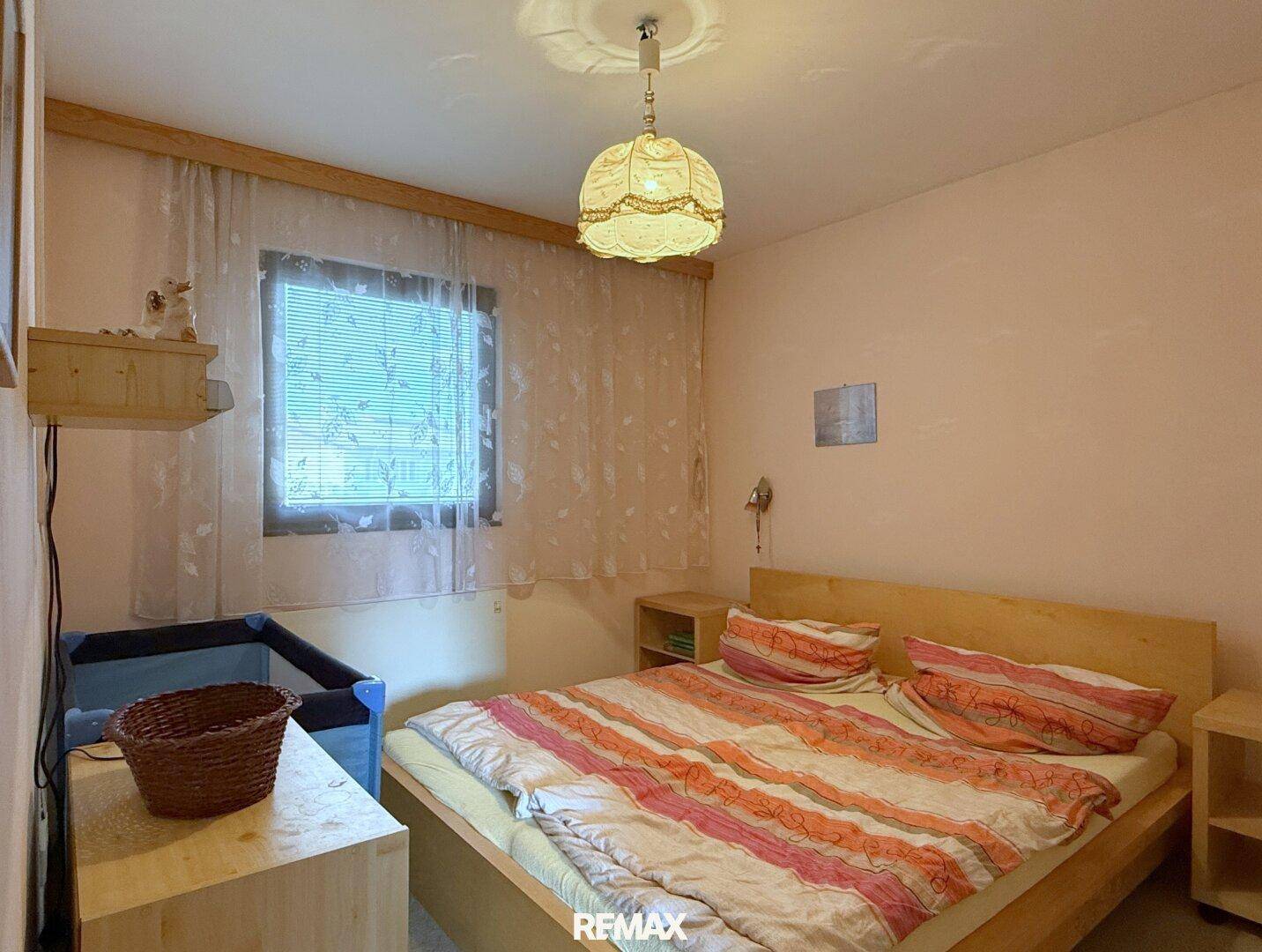 Helles Schlafzimmer mit Doppelbett, Holzmöbeln und einem Babybettchen am Fenster.