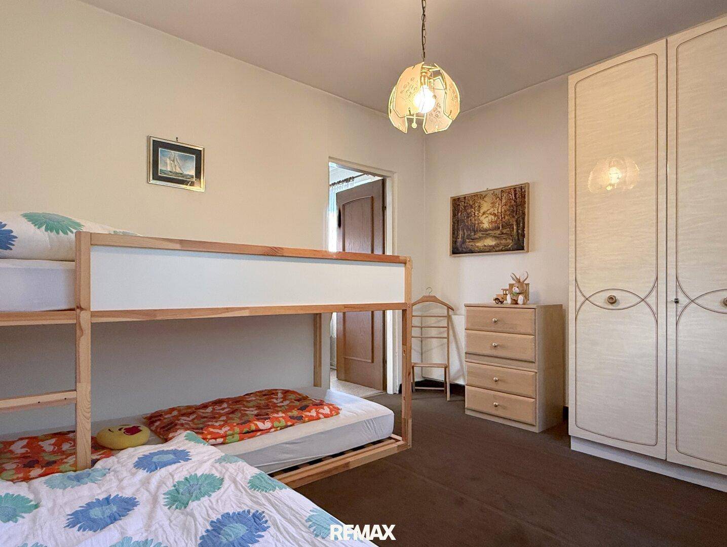 Kinderzimmer mit Etagenbett, weißem Kleiderschrank und Holzboden.