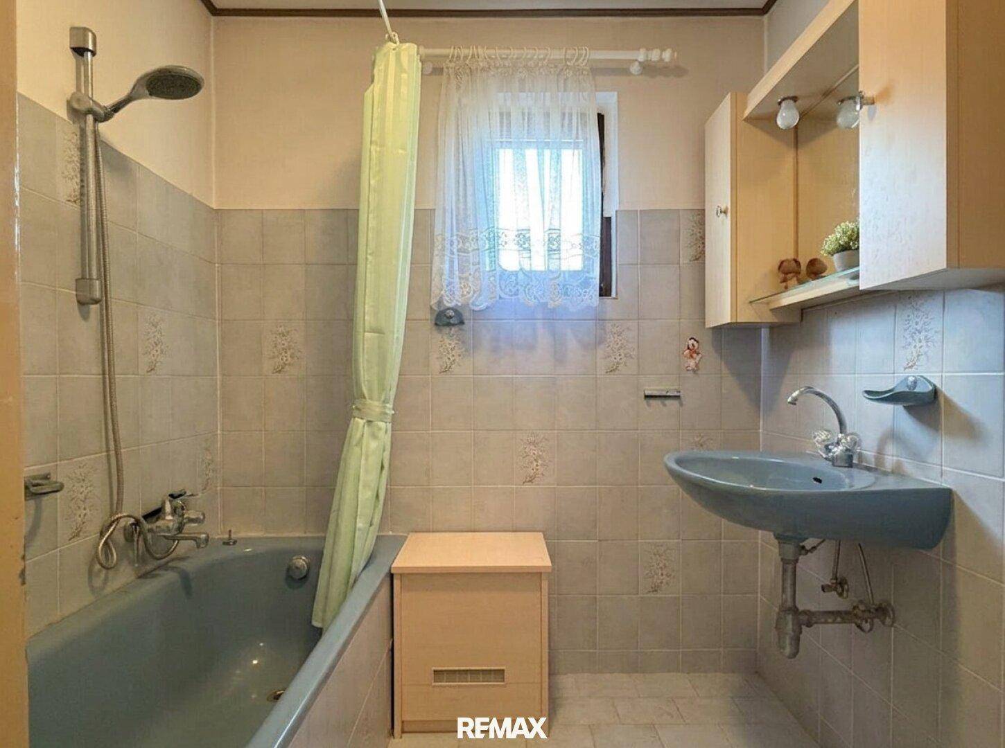 Badezimmer mit Badewanne, Duschvorhang, Waschbecken und hellgrauen Fliesen.