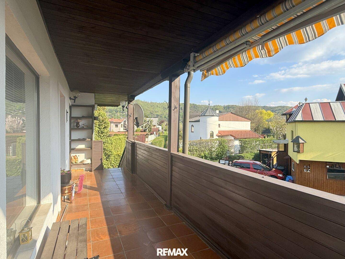 Langer Balkon mit Holzboden, Markise und weitem Blick auf die grüne Umgebung.
