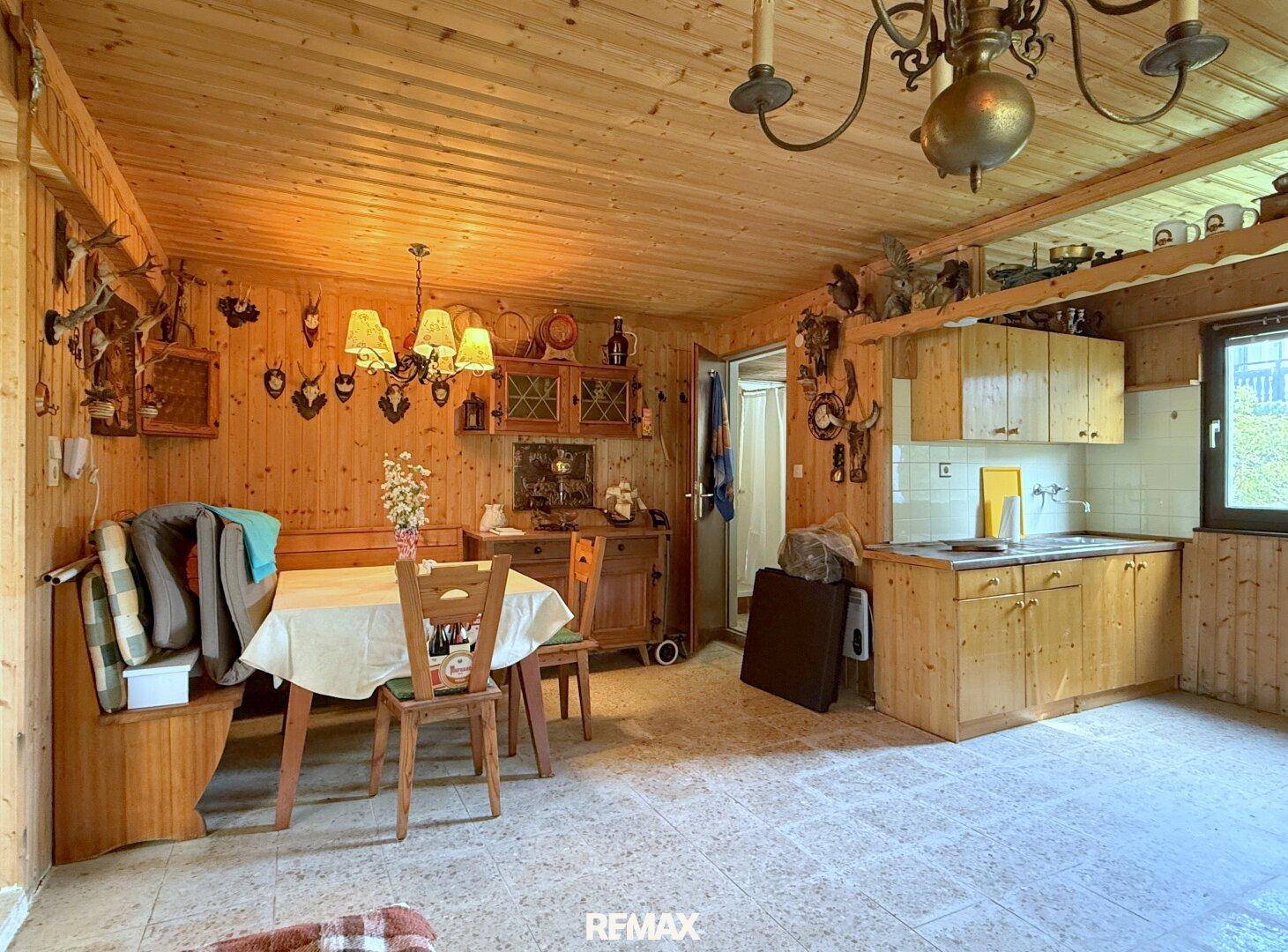 Rustikaler Wohnbereich mit Holztäfelung, Essbereich, kleiner Küchenzeile und Jagdtrophäen.