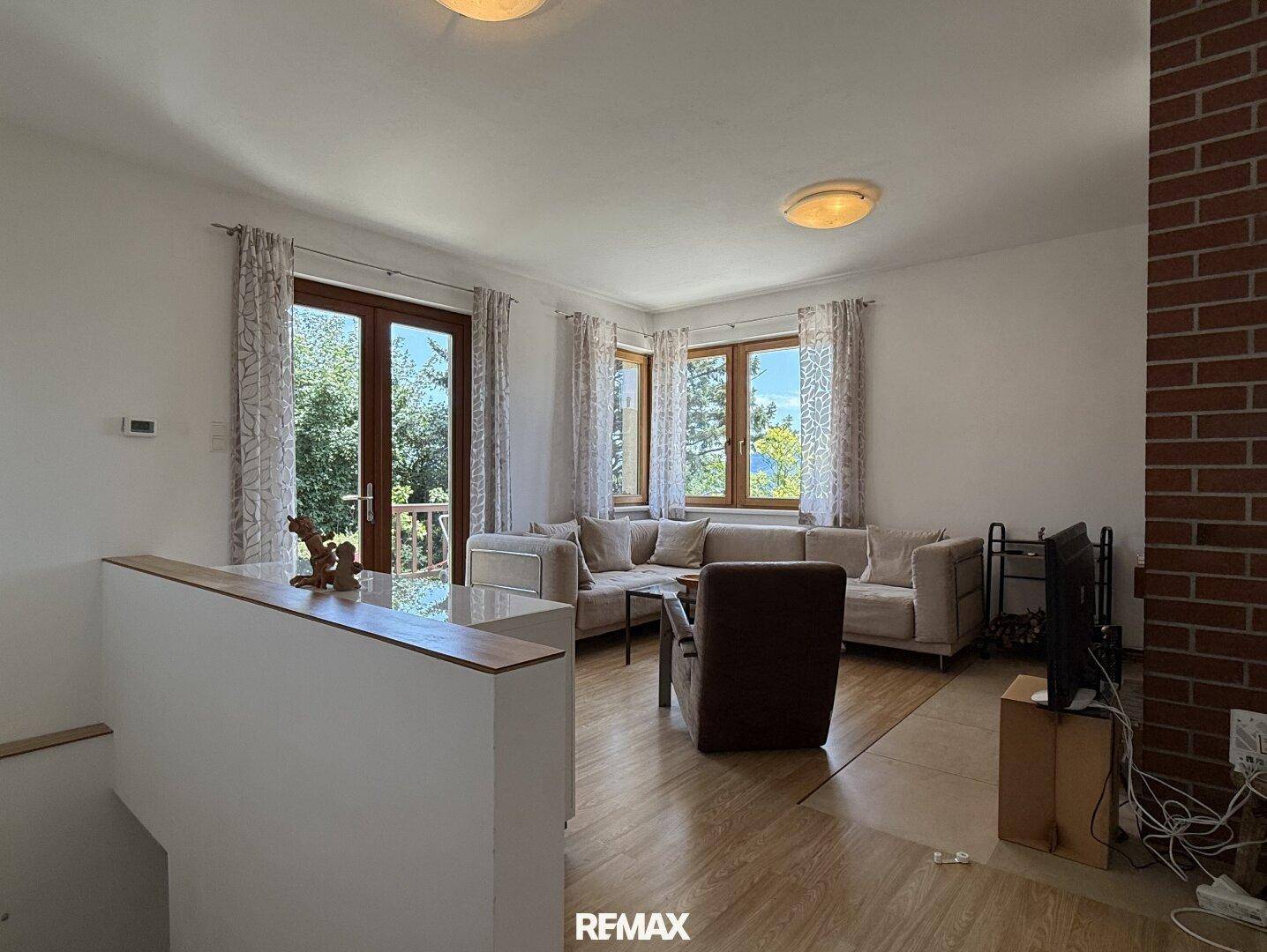 Helles Wohnzimmer mit beigem Ecksofa, Holzboden und Zugang zum Balkon mit Blick ins Grüne.
