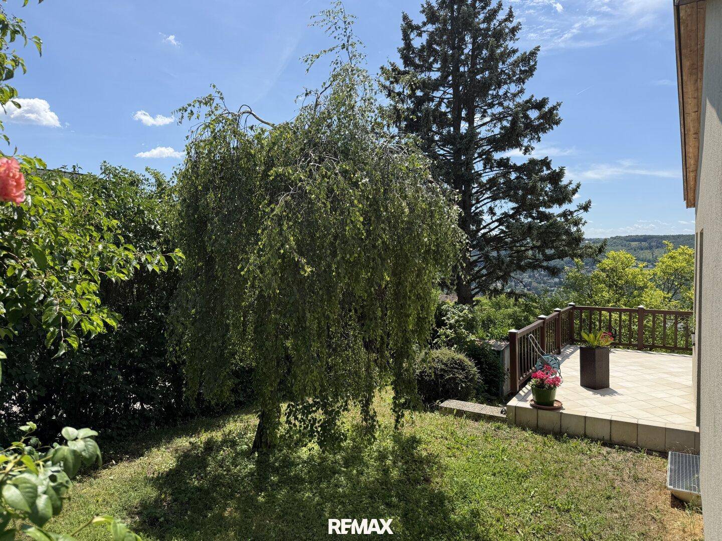 Grüner Gartenbereich mit Bäumen und einer kleinen Terrasse, die zum Entspannen einlädt.