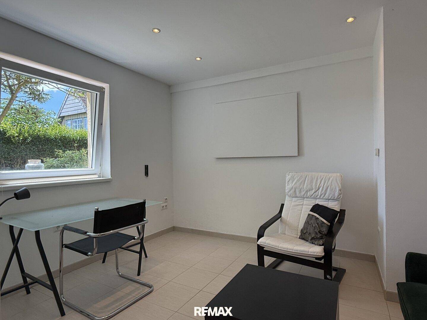 Helles Arbeitszimmer mit Schreibtisch, Sessel und Fenster mit Blick ins Grüne.