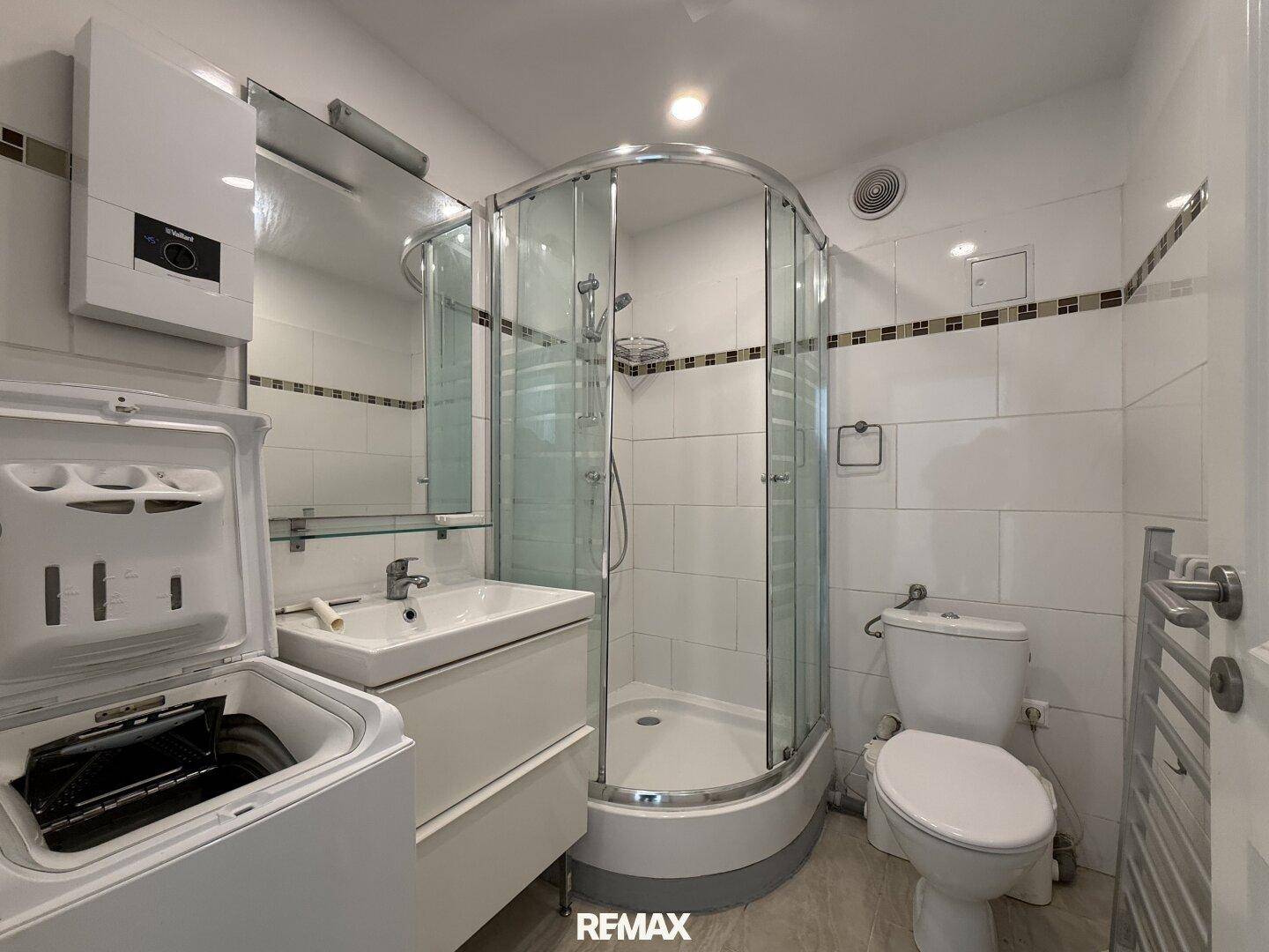 Kleines Badezimmer mit Dusche, WC und Waschbecken, ausgestattet mit einer Waschmaschine.