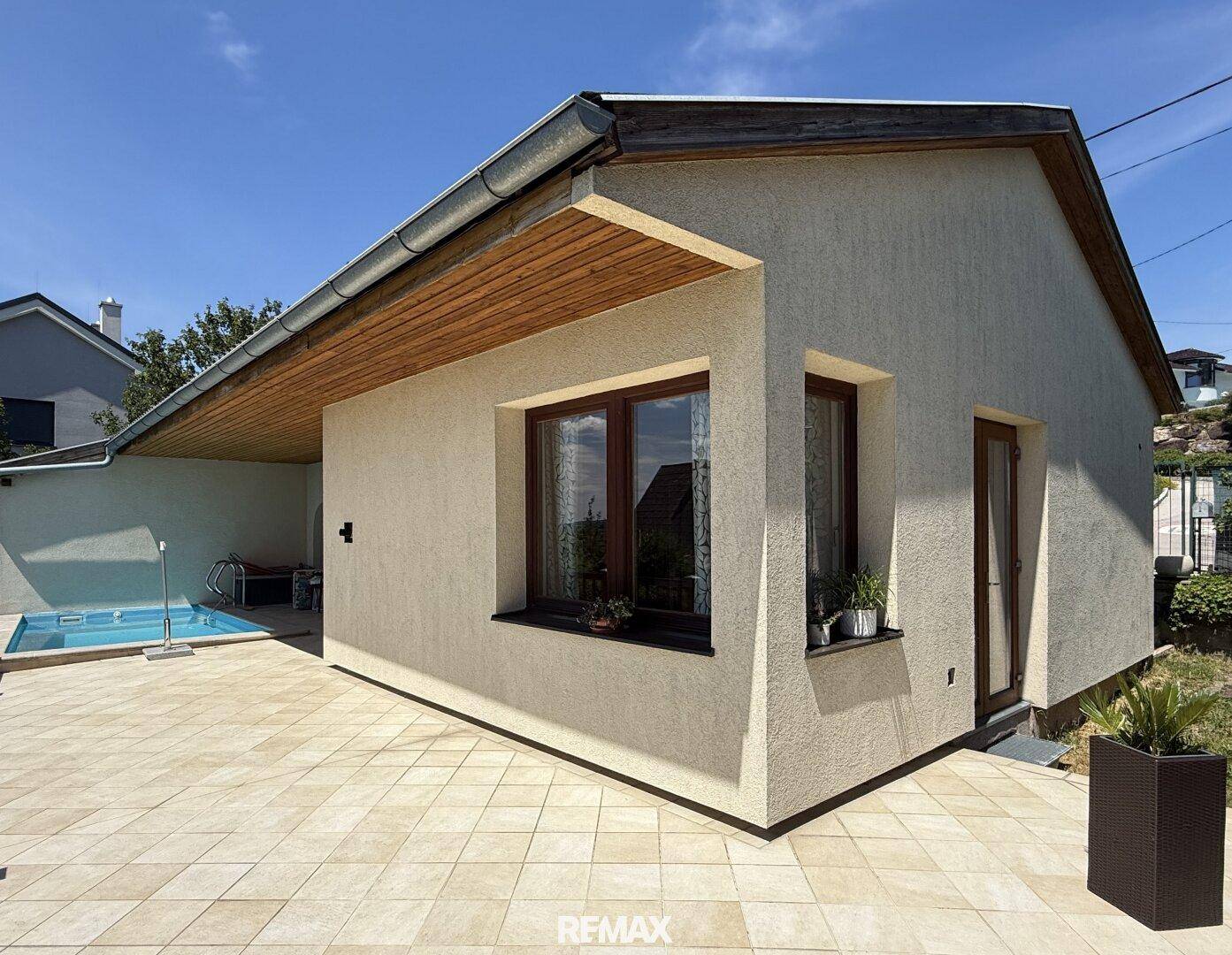 Seitenansicht des Hauses mit Poolbereich und großer, gefliester Terrasse unter blauem Himmel.