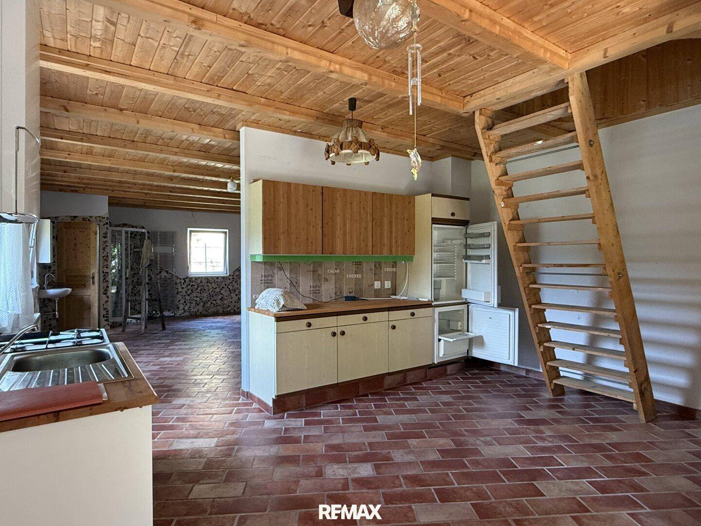 Rustikale Küche mit Holzdecke, Terrakottafliesen und einer einfachen Küchenzeile mit Kühlschrank und Leiter.