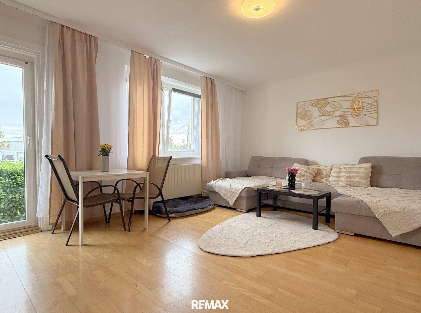 Helles Wohnzimmer mit Parkettboden, beigem Sofa und Zugang zum Außenbereich.