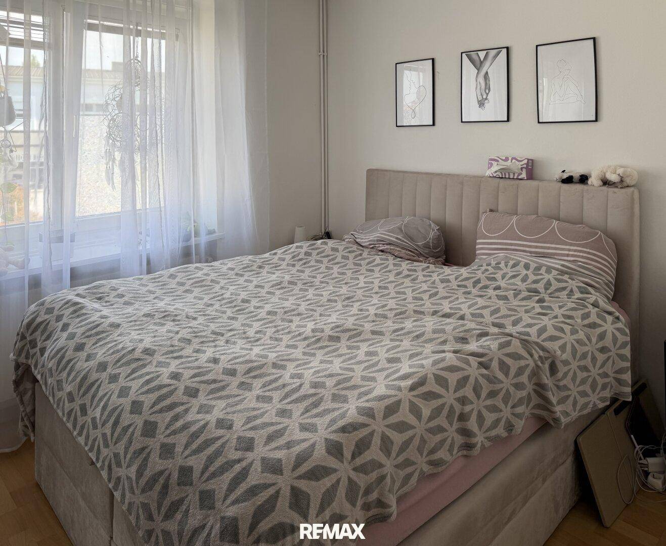 Helles Schlafzimmer mit großem Bett, Holzboden und modernen gerahmten Bildern an der Wand.