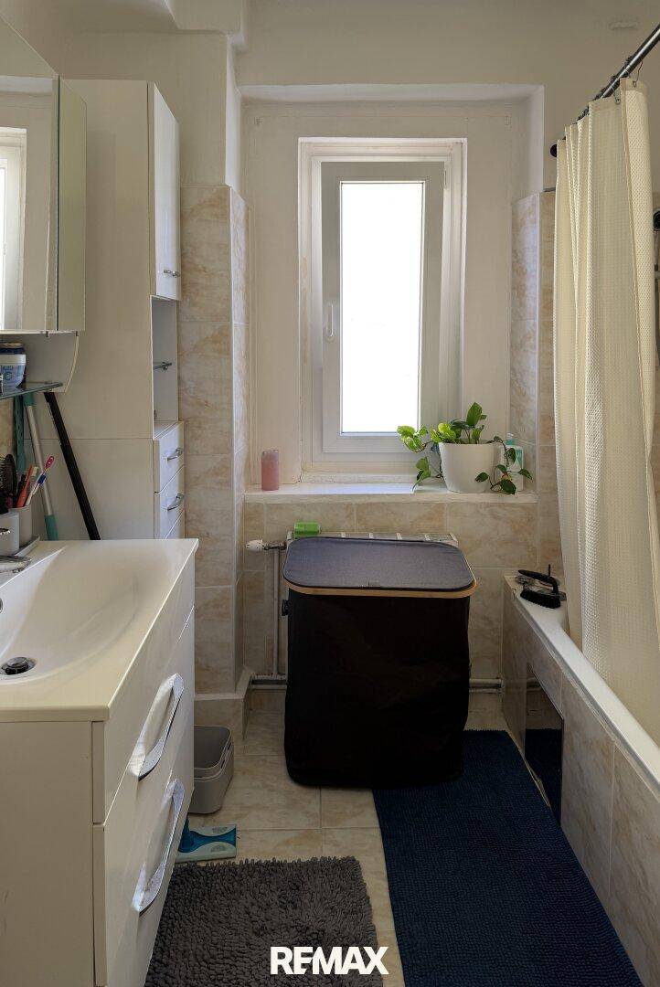 Badezimmer mit Badewanne, Waschbecken, Spiegelschrank und Fenster für Tageslicht.