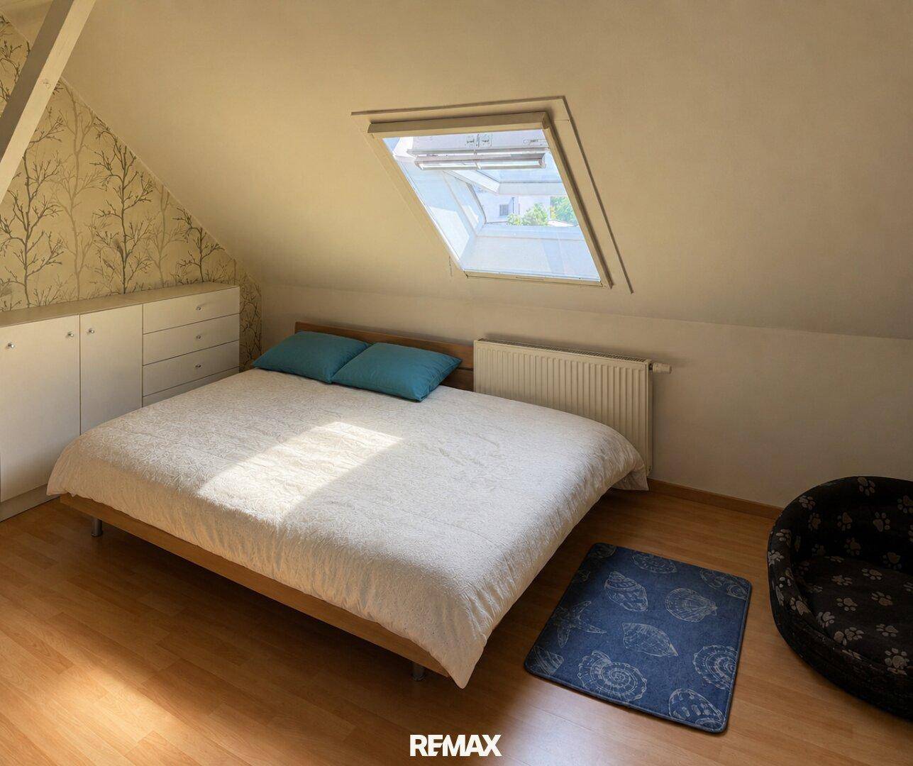 Gemütliches Schlafzimmer im Dachgeschoss mit Dachfenster, Holzboden und Schränken.