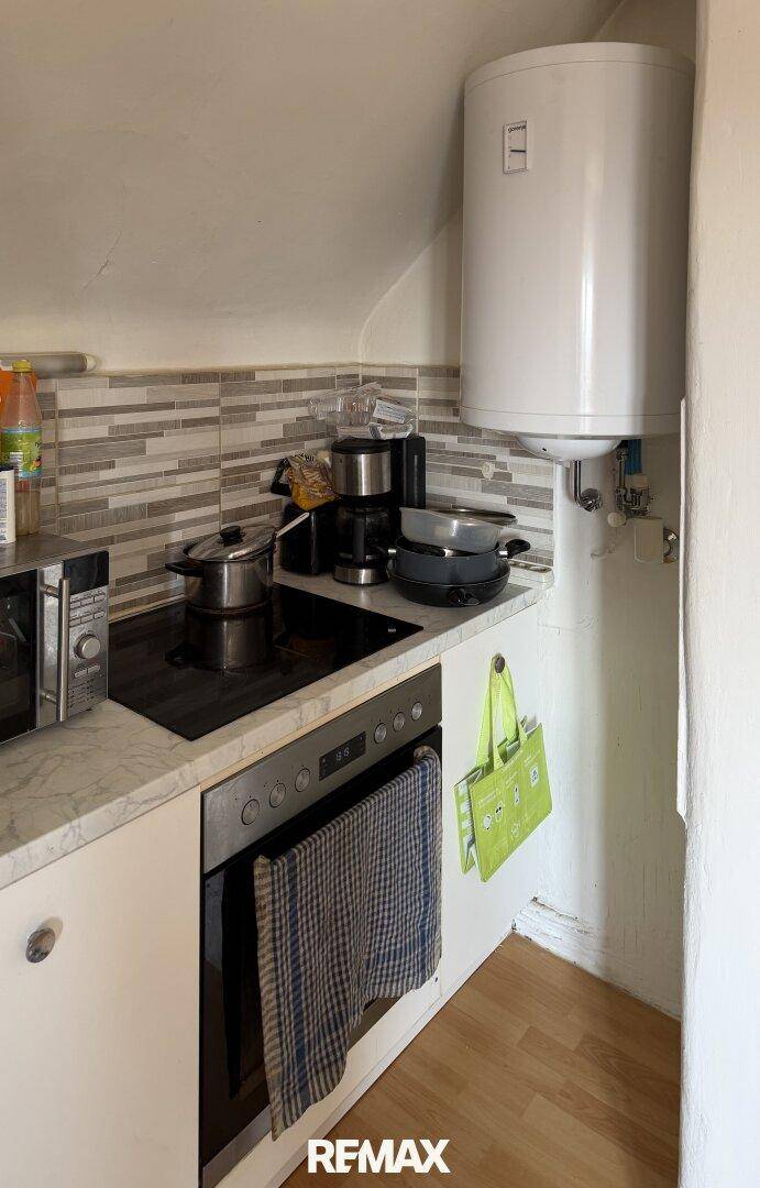 Kleine Küche mit Kochfeld, Backofen und Warmwasserboiler, ideal für eine Kochnische.