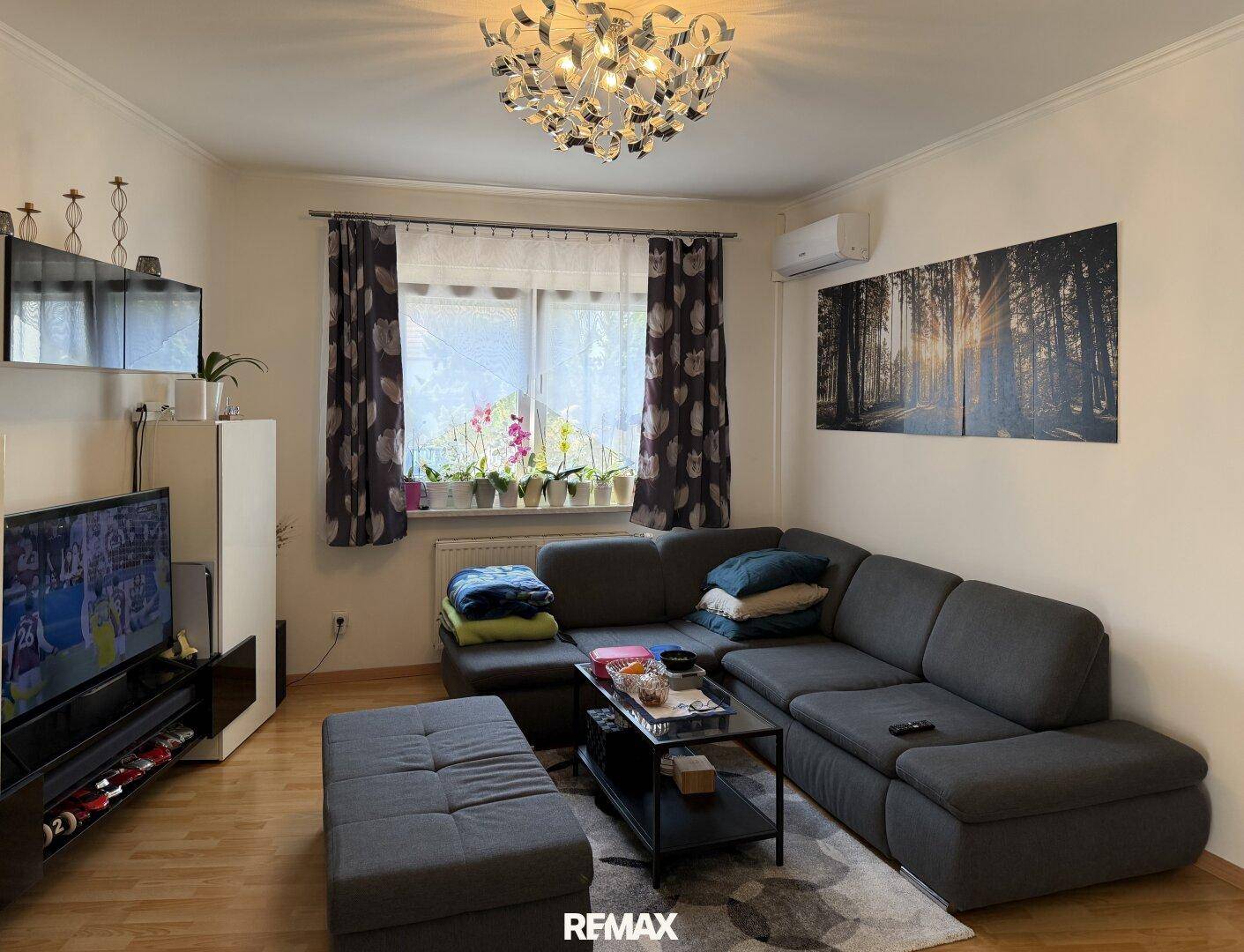 Modern eingerichtetes Wohnzimmer mit großem Ecksofa, Fernseher und Klimaanlage.