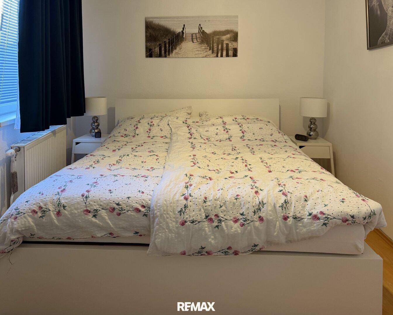 Schlafzimmer mit weißem Doppelbett, floraler Bettwäsche und Nachttischen mit Lampen.