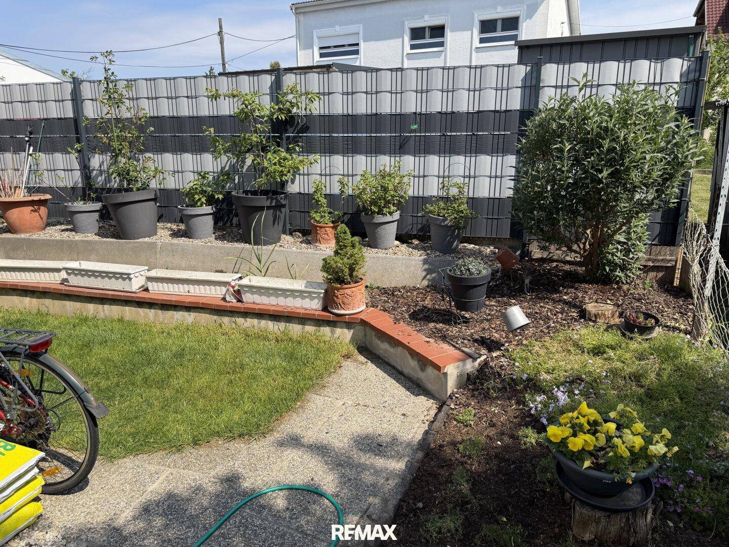 Gepflegter Gartenbereich mit verschiedenen Pflanzen, Töpfen und einem Zaun.