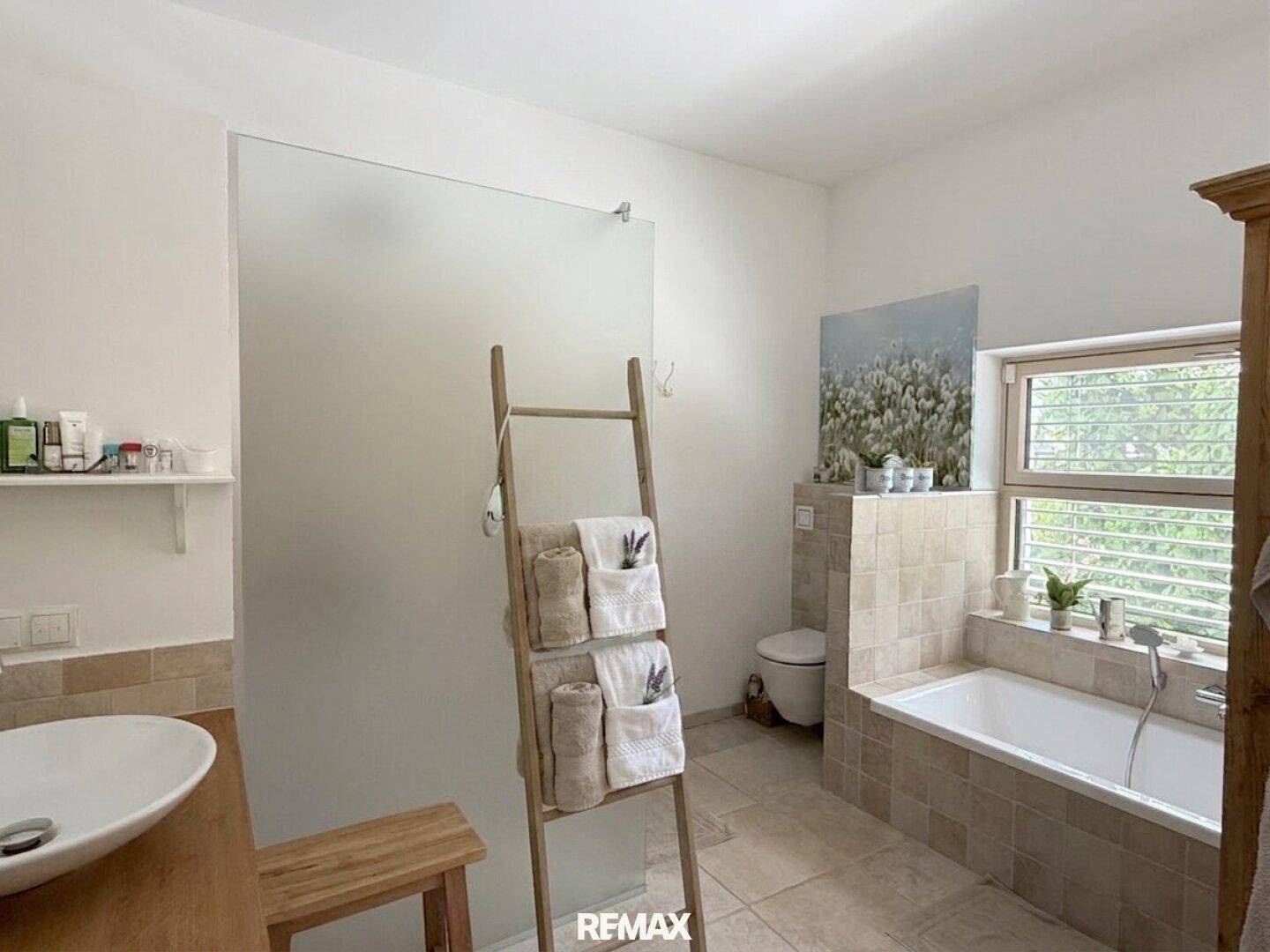 Geräumiges Badezimmer mit Dusche, Badewanne und Fenster, in warmen Farbtönen.
