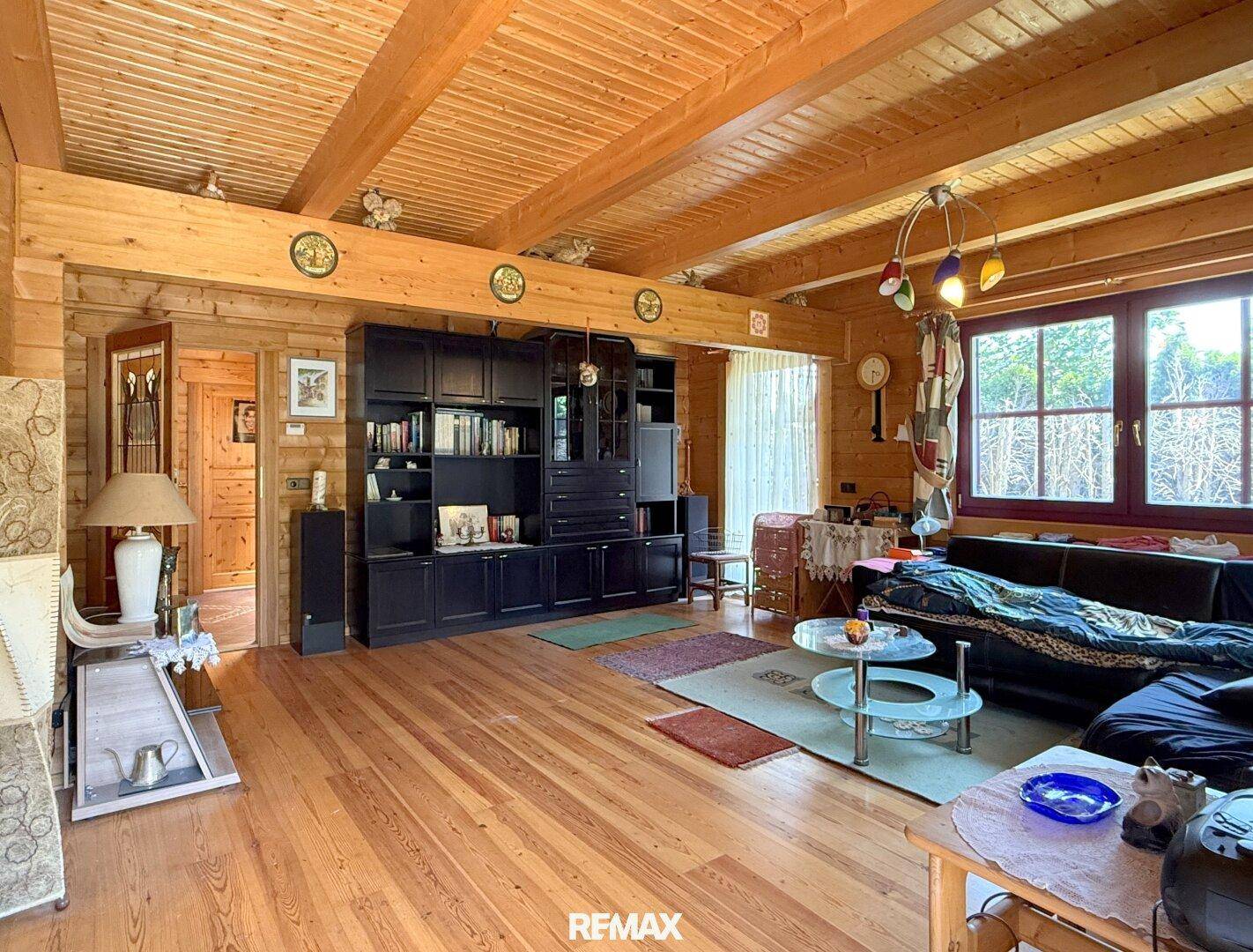 Geräumiges Wohnzimmer mit Holzboden, sichtbaren Deckenbalken und dunklem Bücherregal.