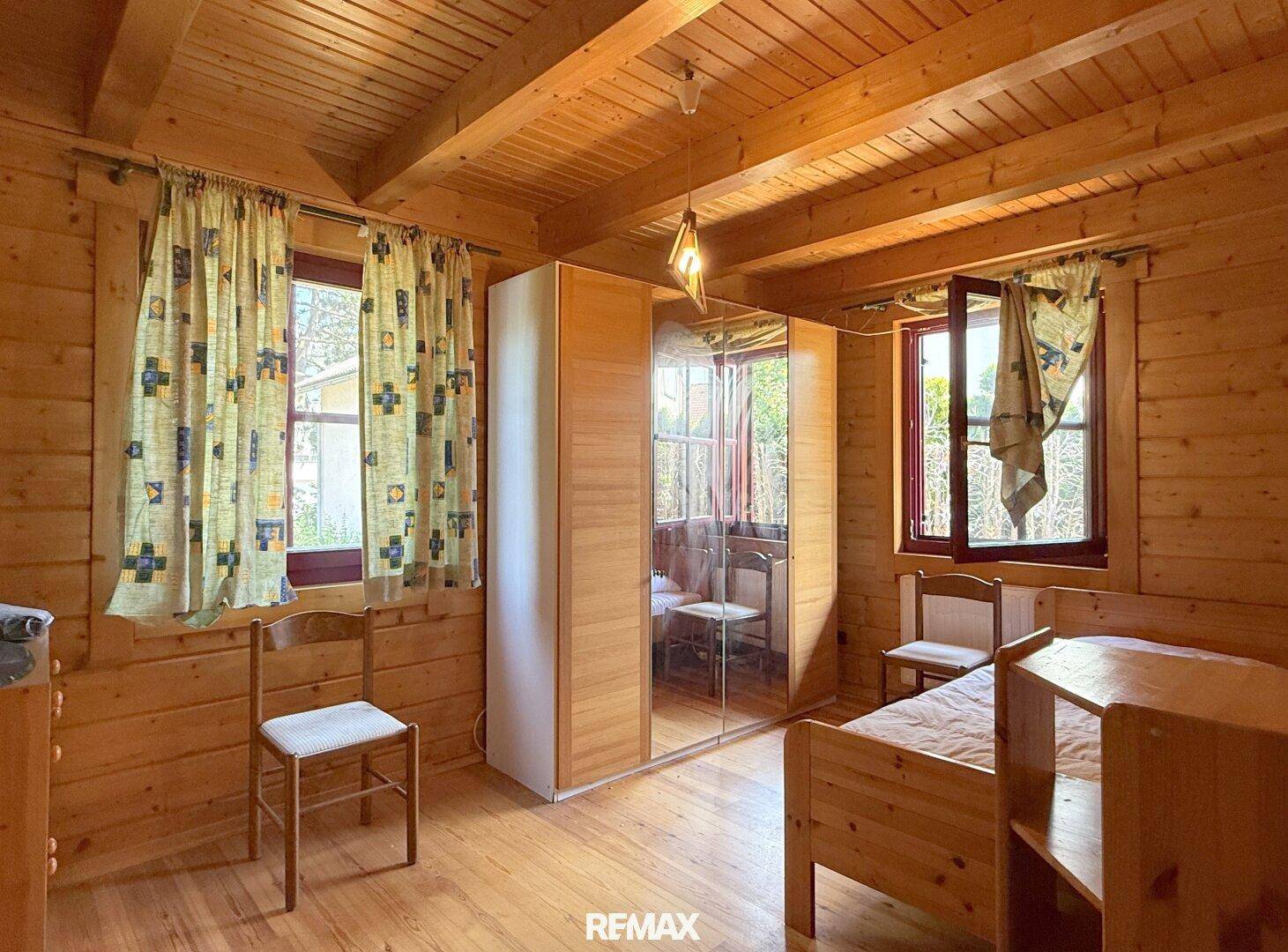 Schlafzimmer mit Holzwänden, Holzboden und einem Kleiderschrank mit Spiegeltüren.