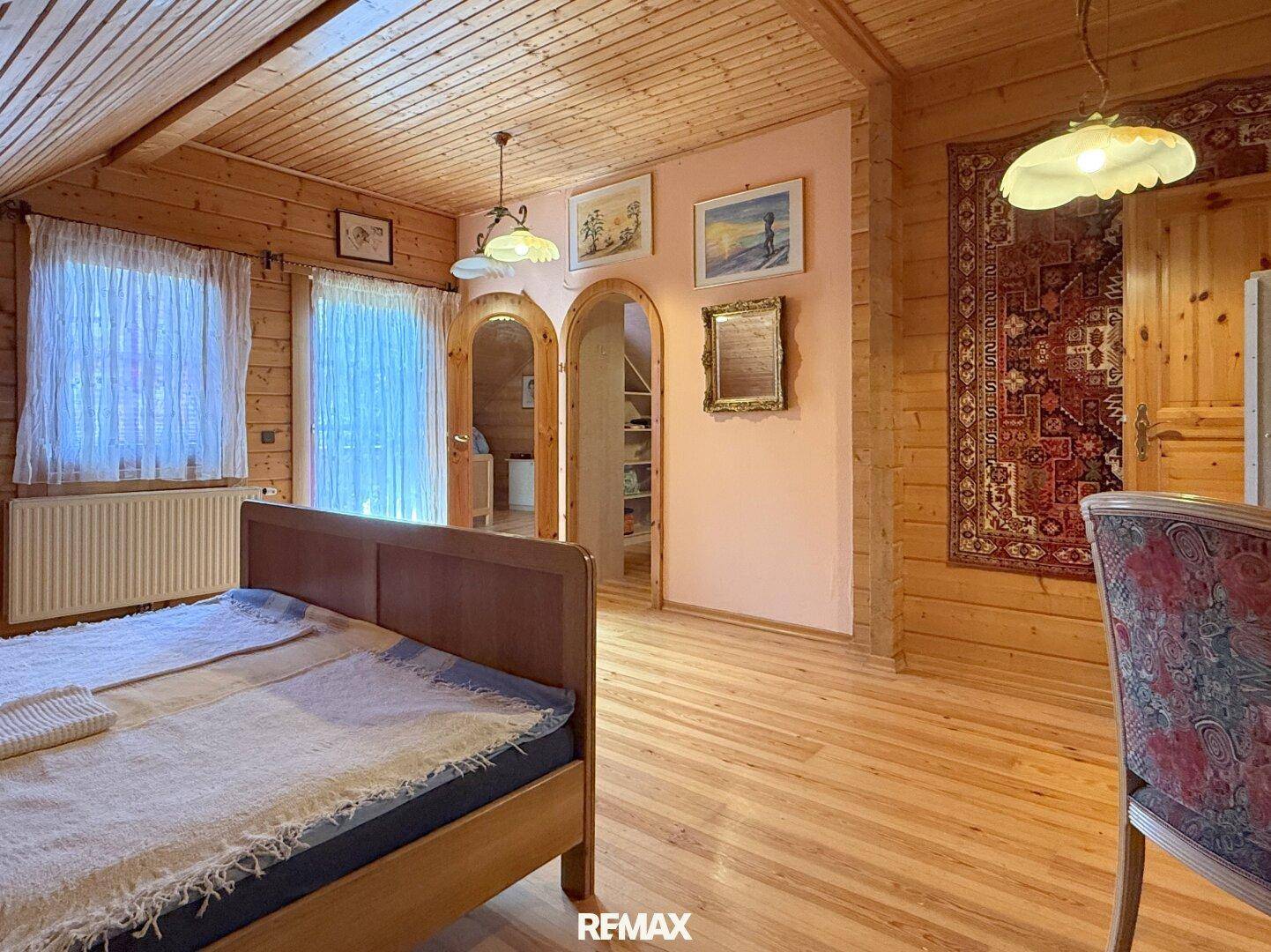 Schlafzimmer mit Holzwänden, Holzboden und einem Teppich als Wanddekoration.