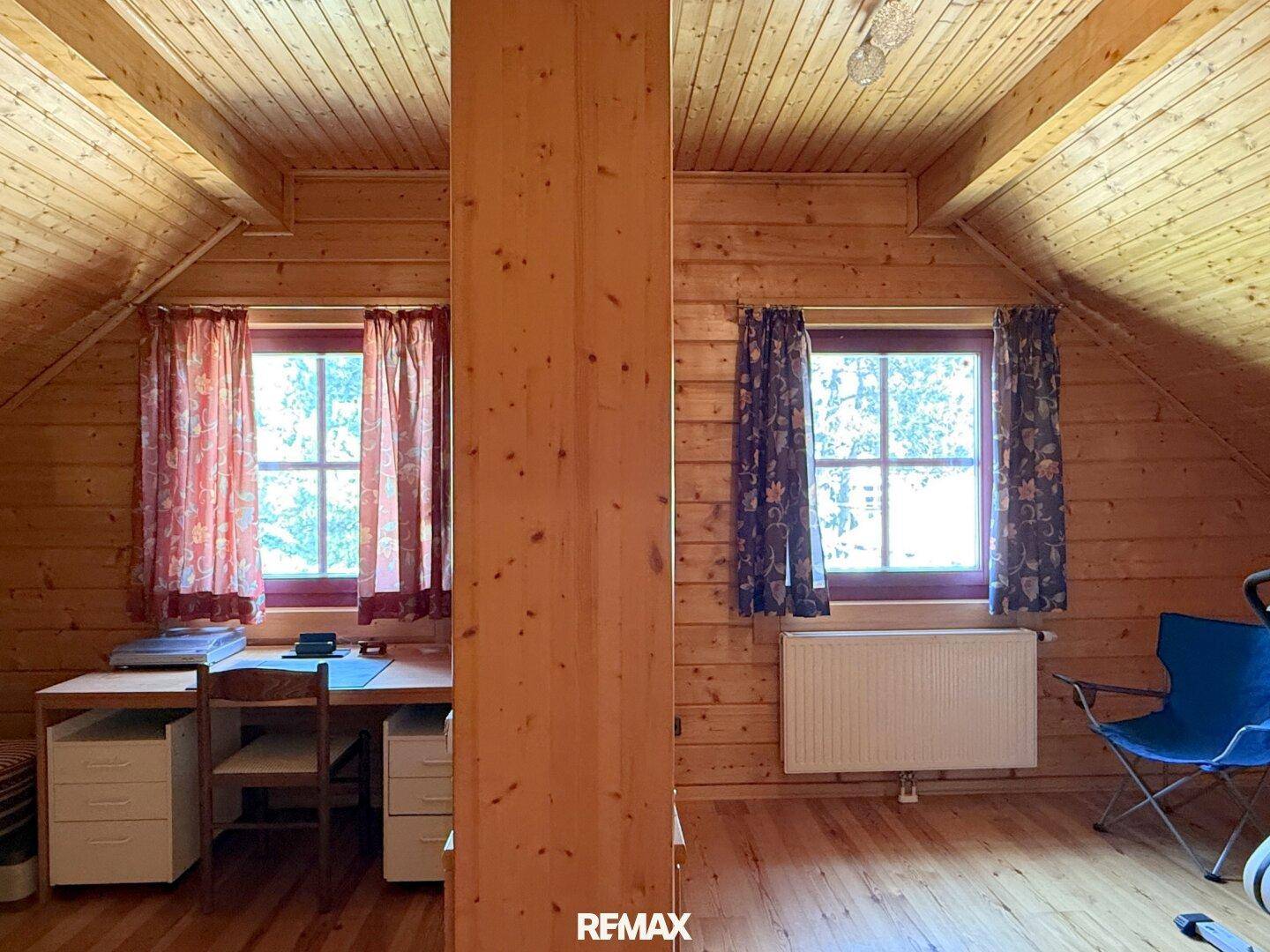 Dachzimmer mit Holzwänden, Holzboden und zwei Fenstern für natürliches Licht.